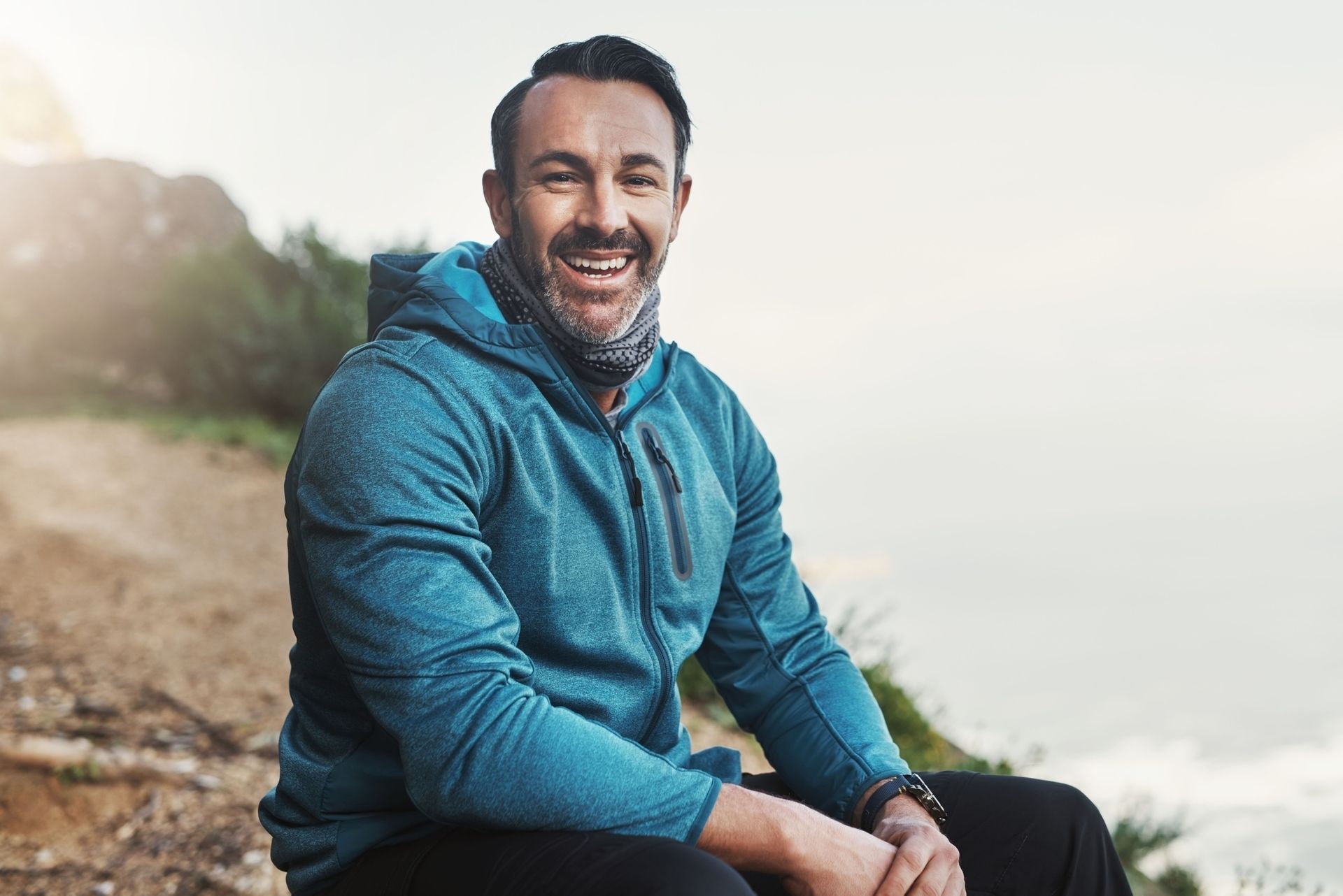 Man in blue hoodie, smiling, outdoors.