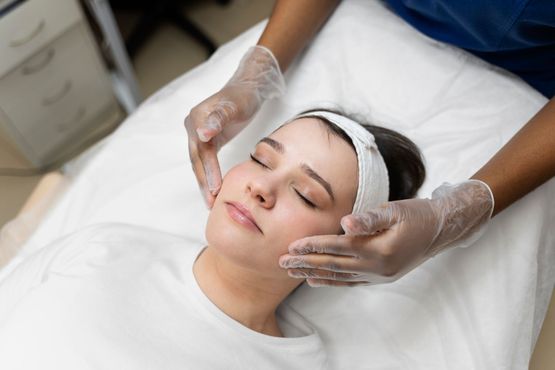 Person receiving facial treatment, face massaged by gloved hands, white bed, interior setting.