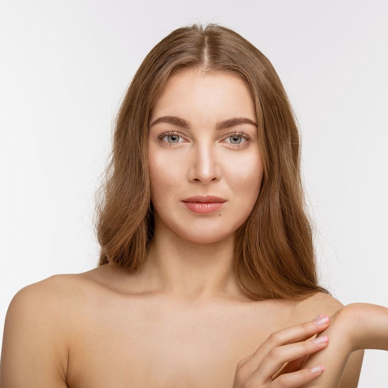 Woman with long brown hair and fair skin, looking towards the viewer. She's touching her arm.