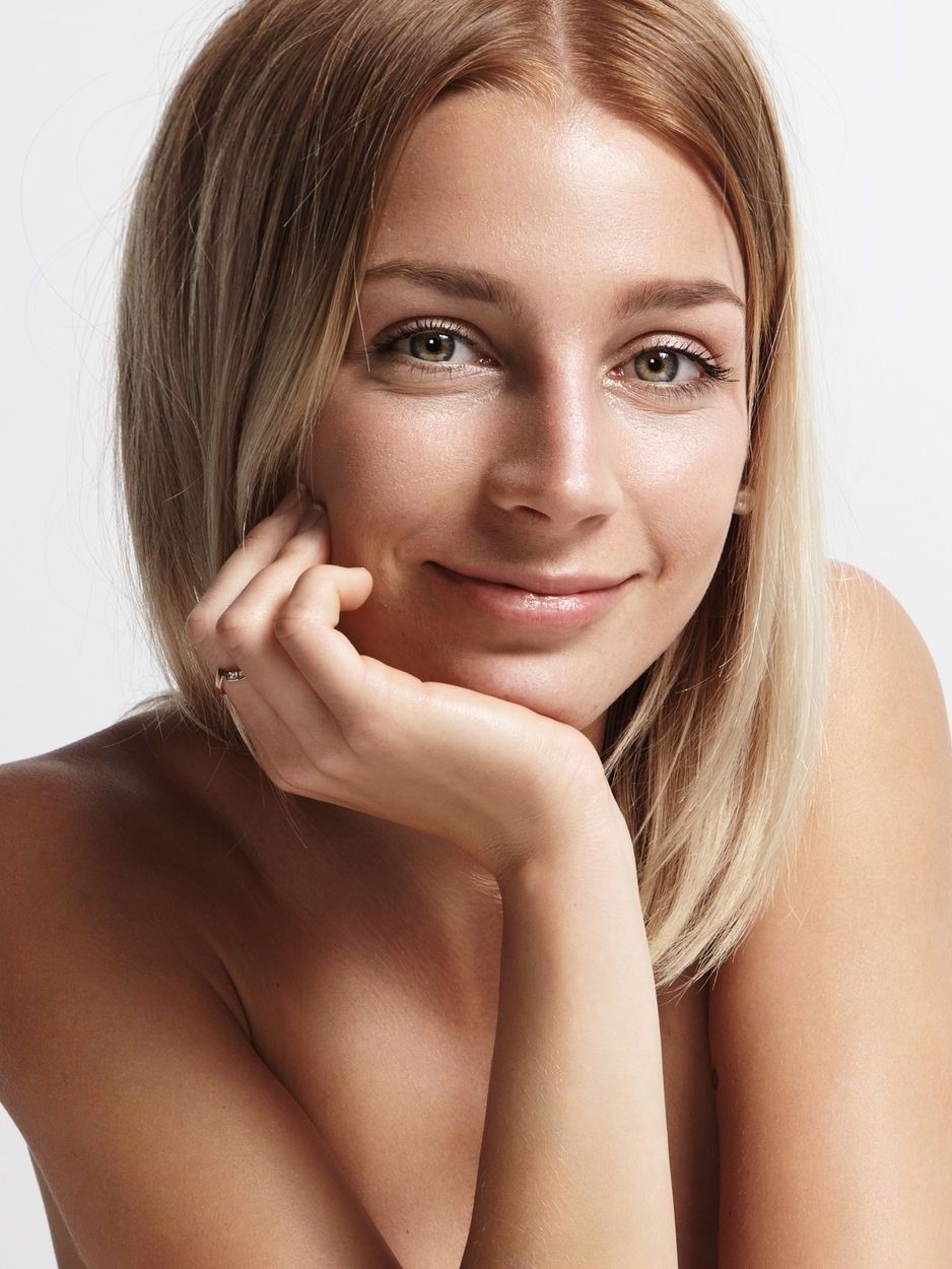Blond woman with green eyes, resting her chin on her hand, smiling softly.