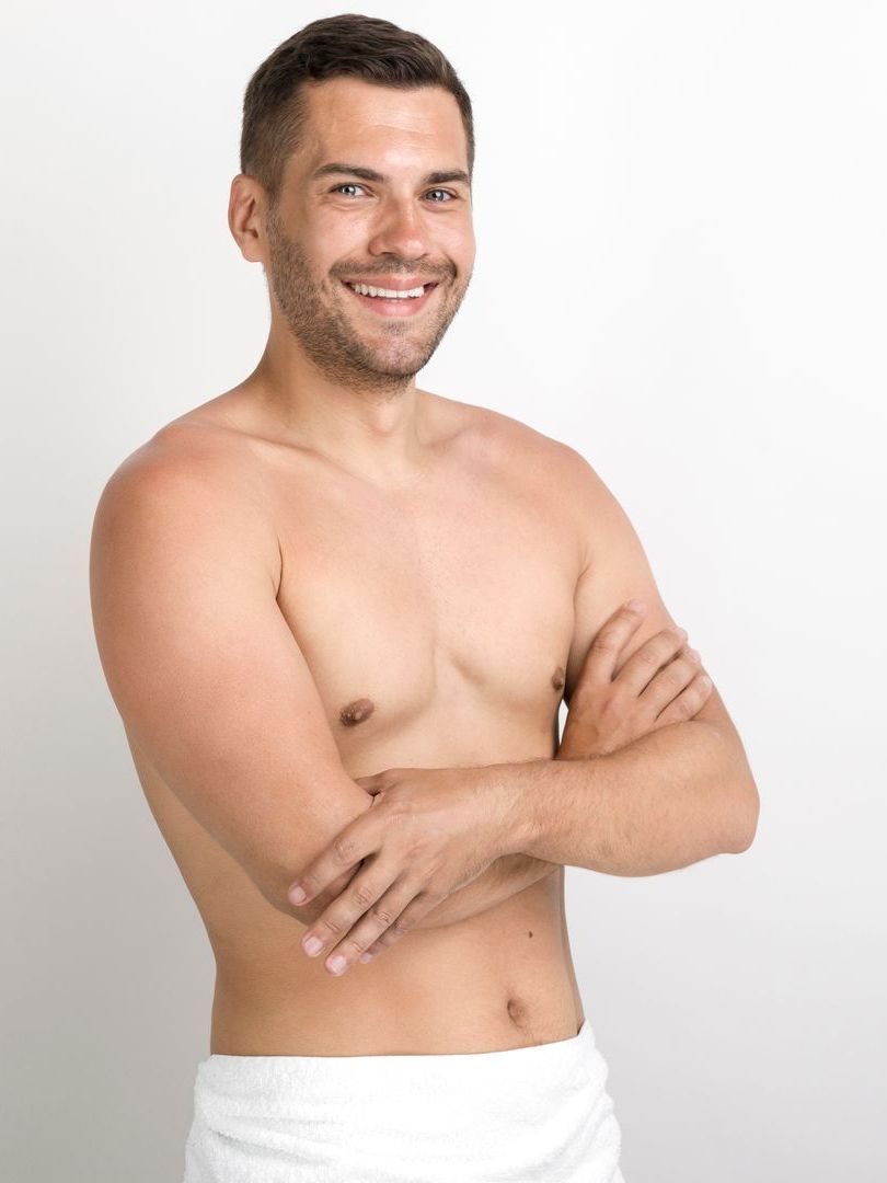 Shirtless man with arms crossed, smiling, against white background.