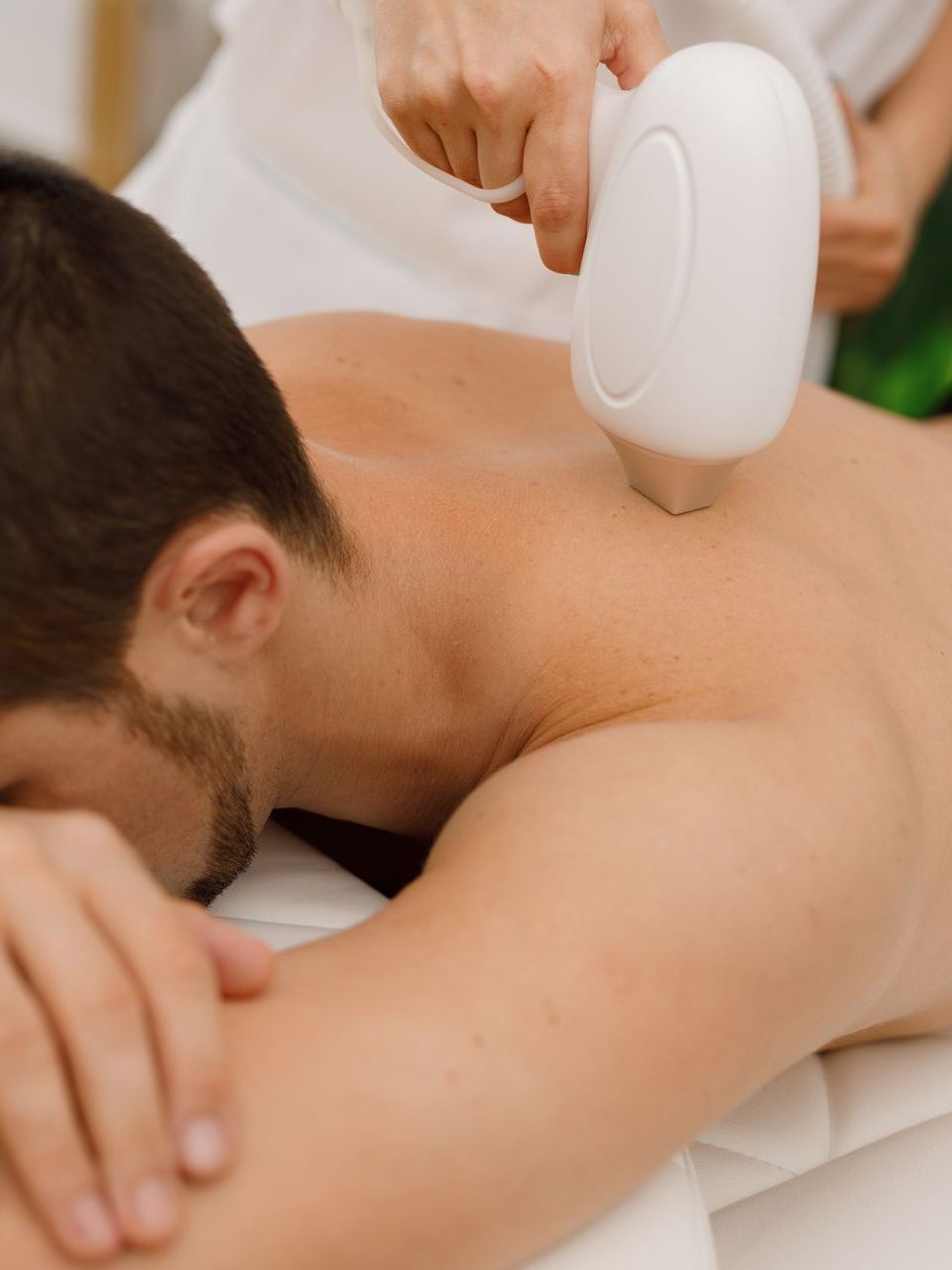 Man receiving laser hair removal on his back at a spa.