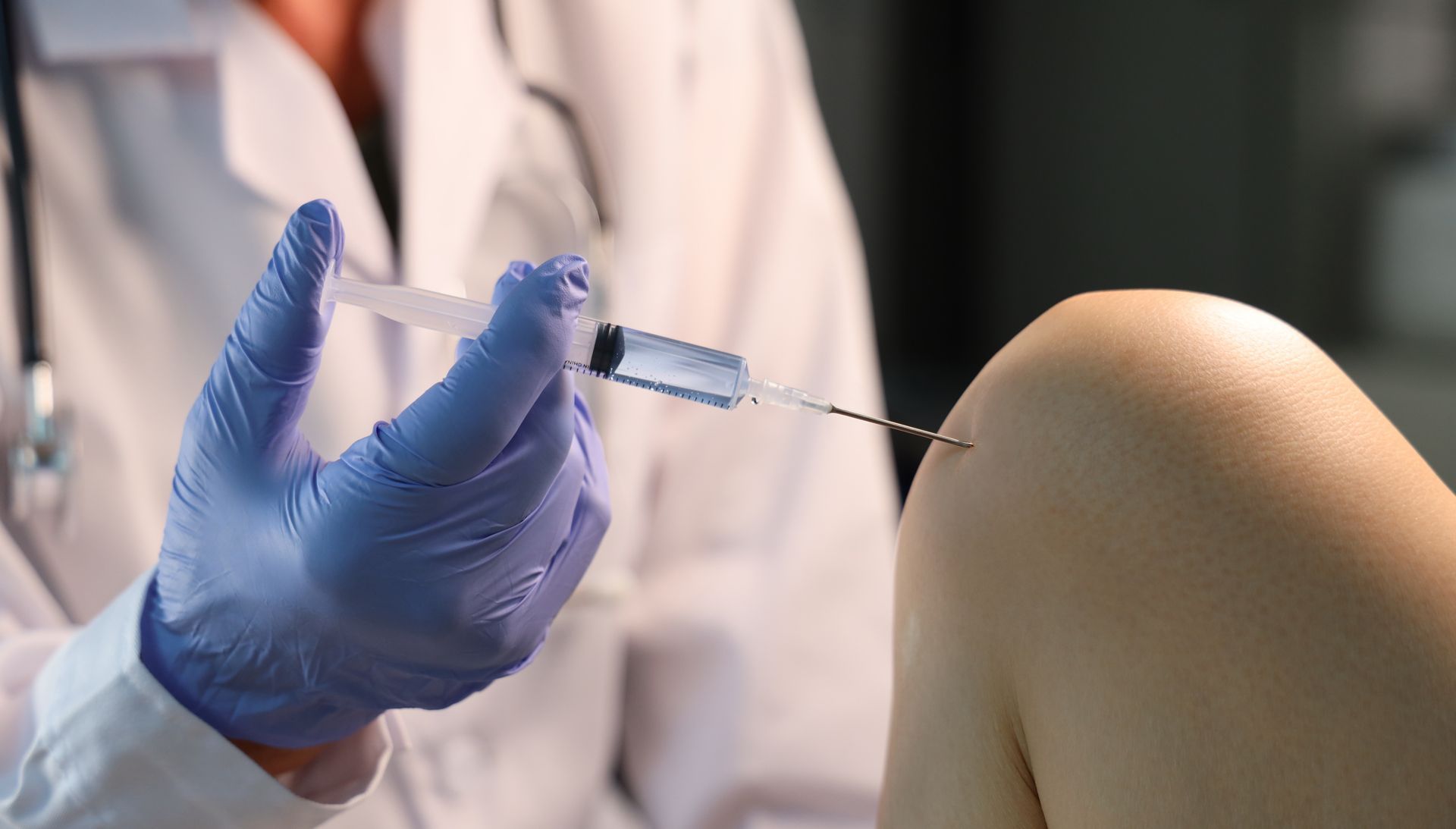 Doctor injecting a syringe into a patient's knee, blue glove and white coat, indoors.