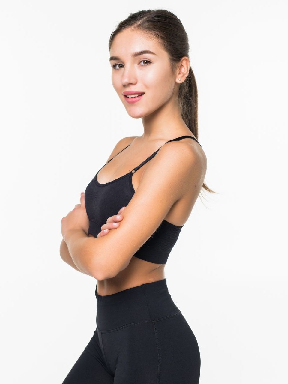 Woman in black activewear, arms crossed, smiling, studio shot.