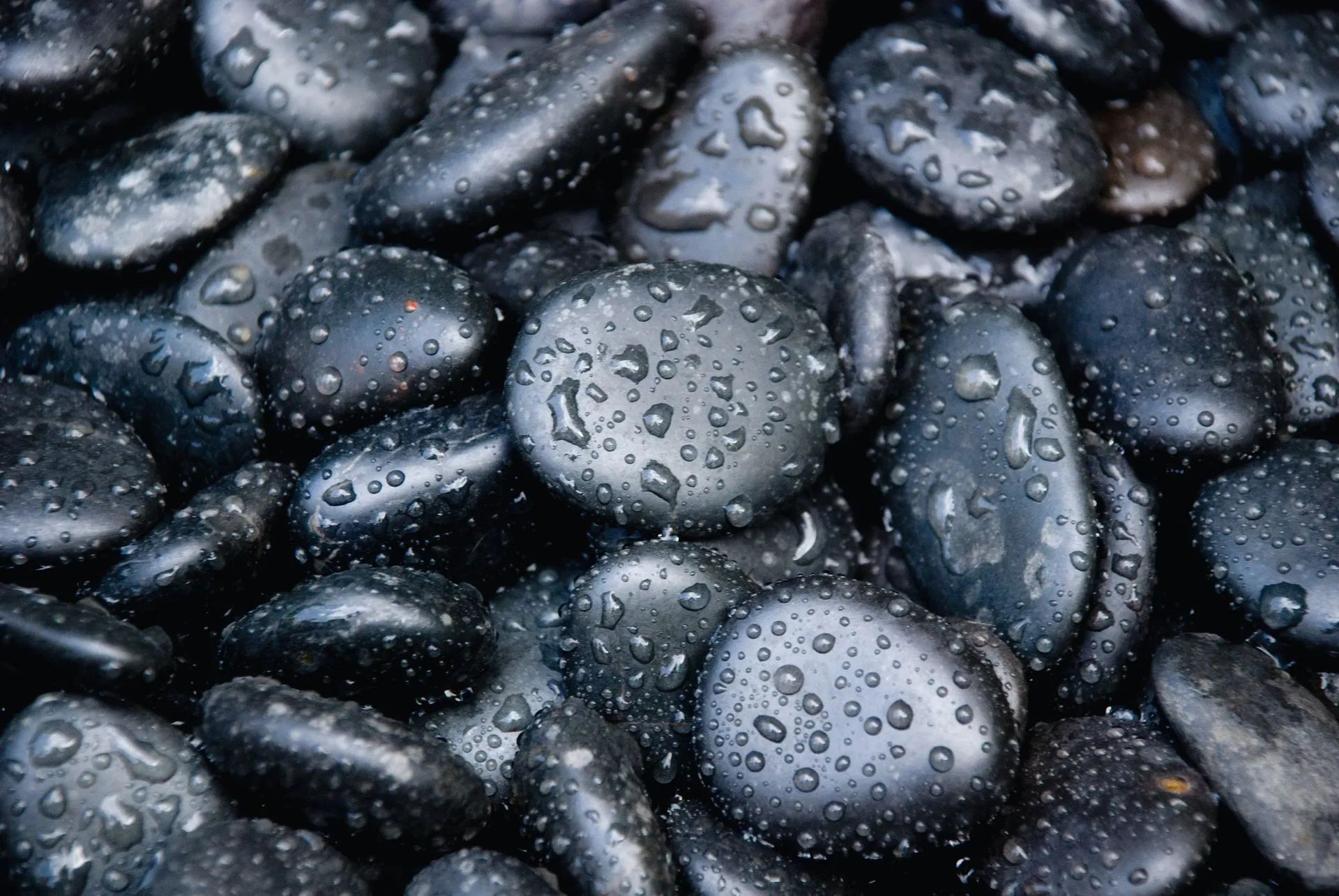 Black, wet river stones with water droplets scattered across the surface.