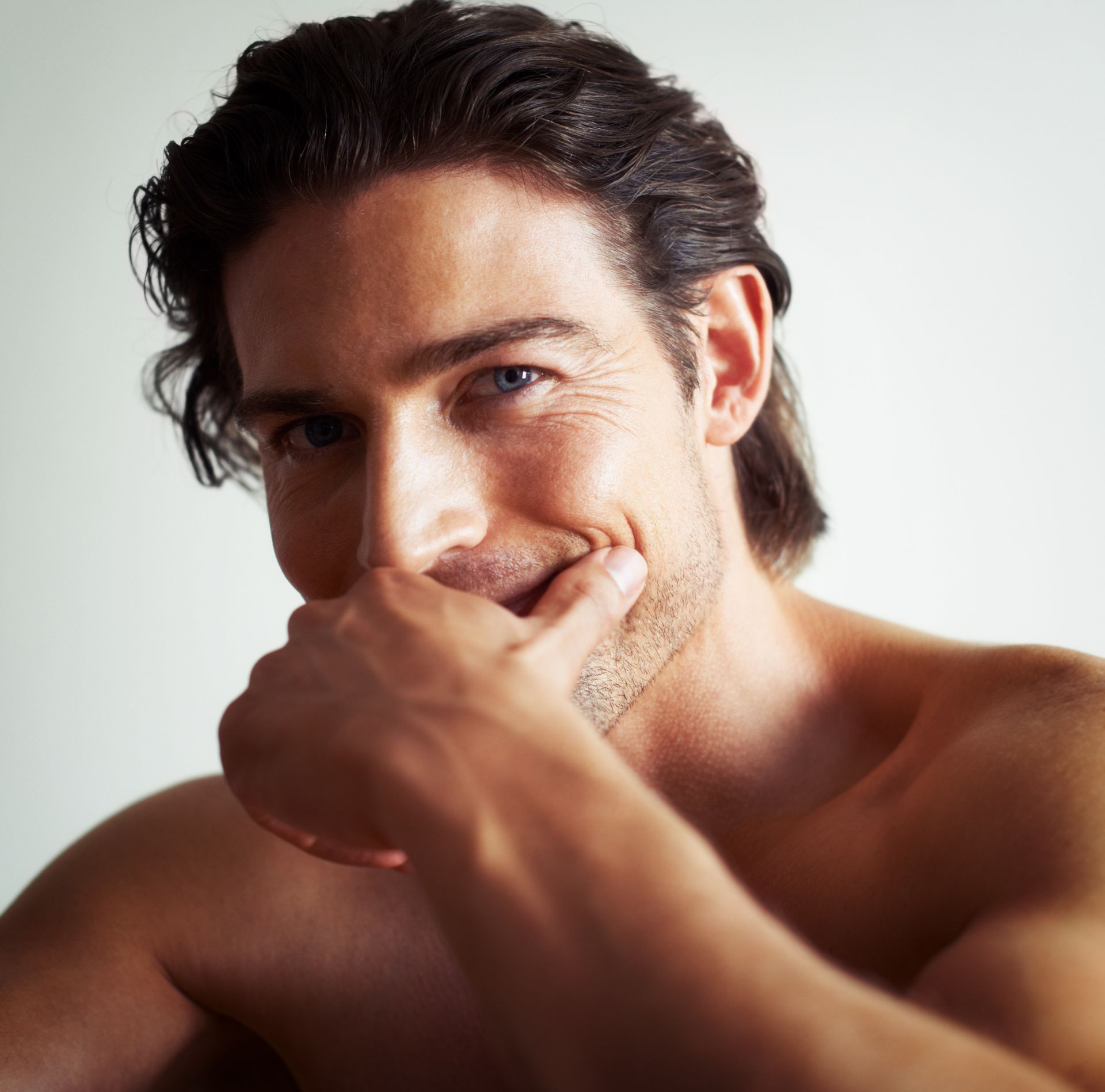 Man with dark hair, smiling, hand near his mouth.