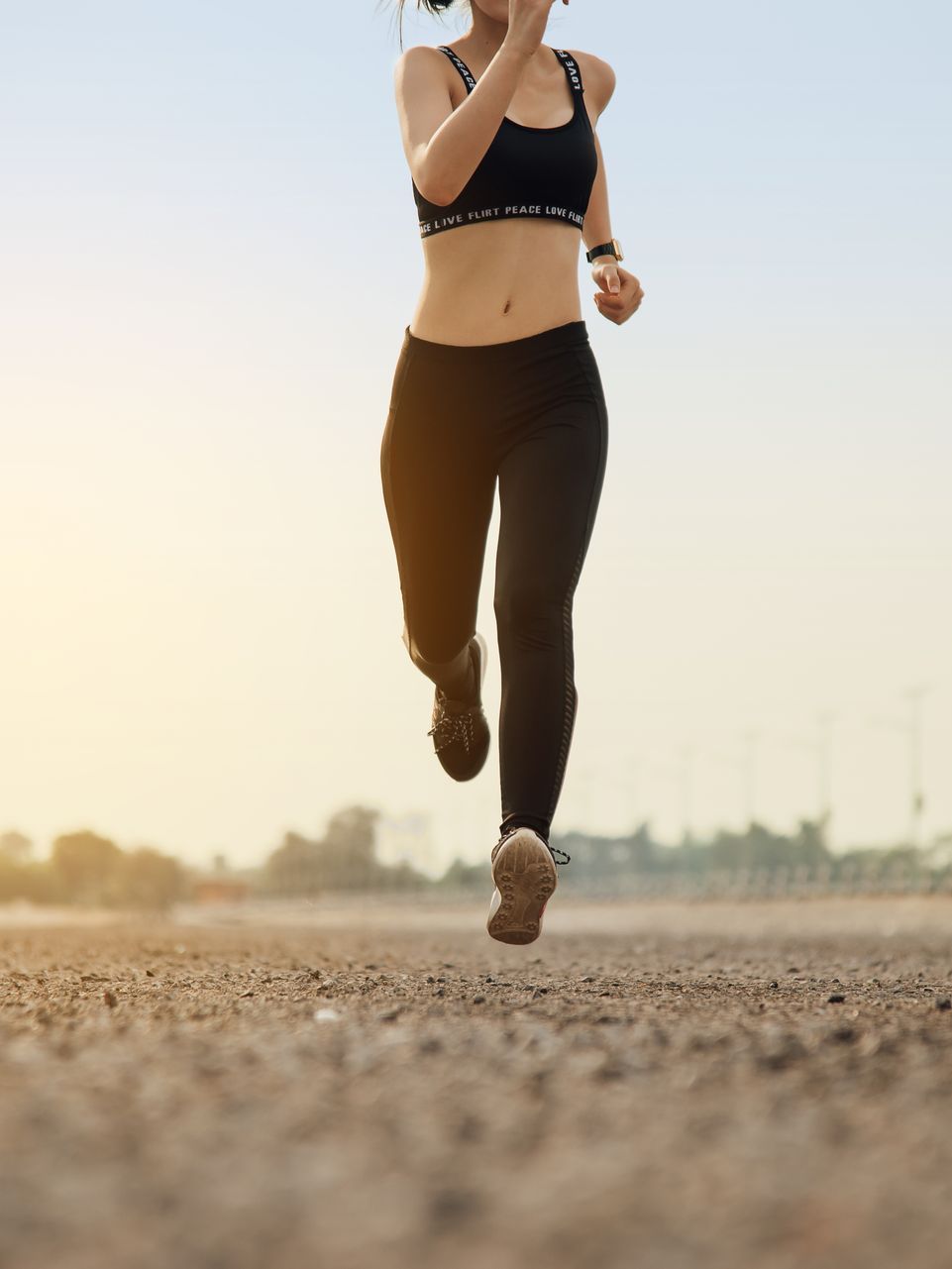 Woman running on a road in athletic wear; early morning, golden sunlight.