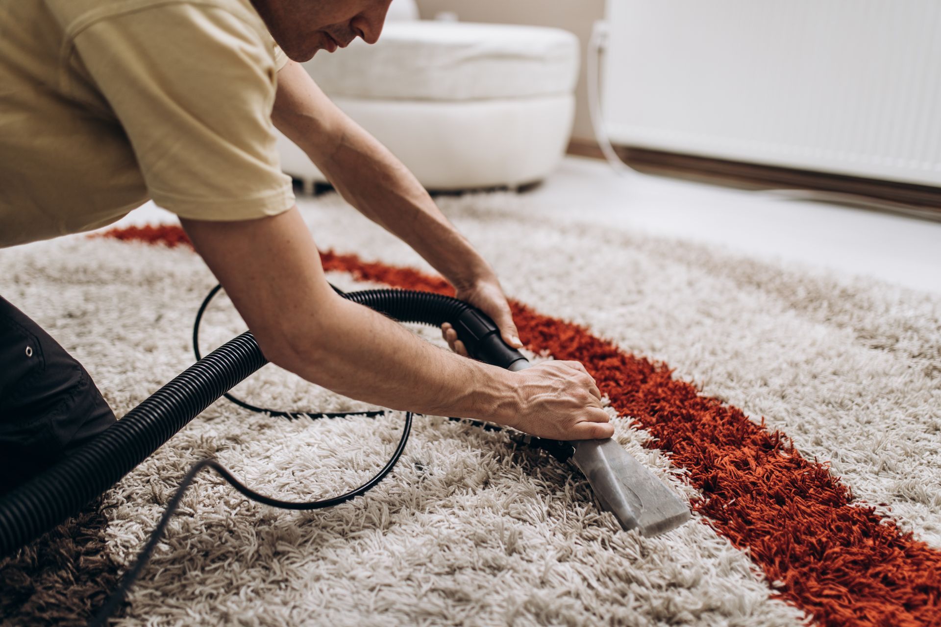 Person cleaning a white shag rug with a vacuum, removing a red spill stain