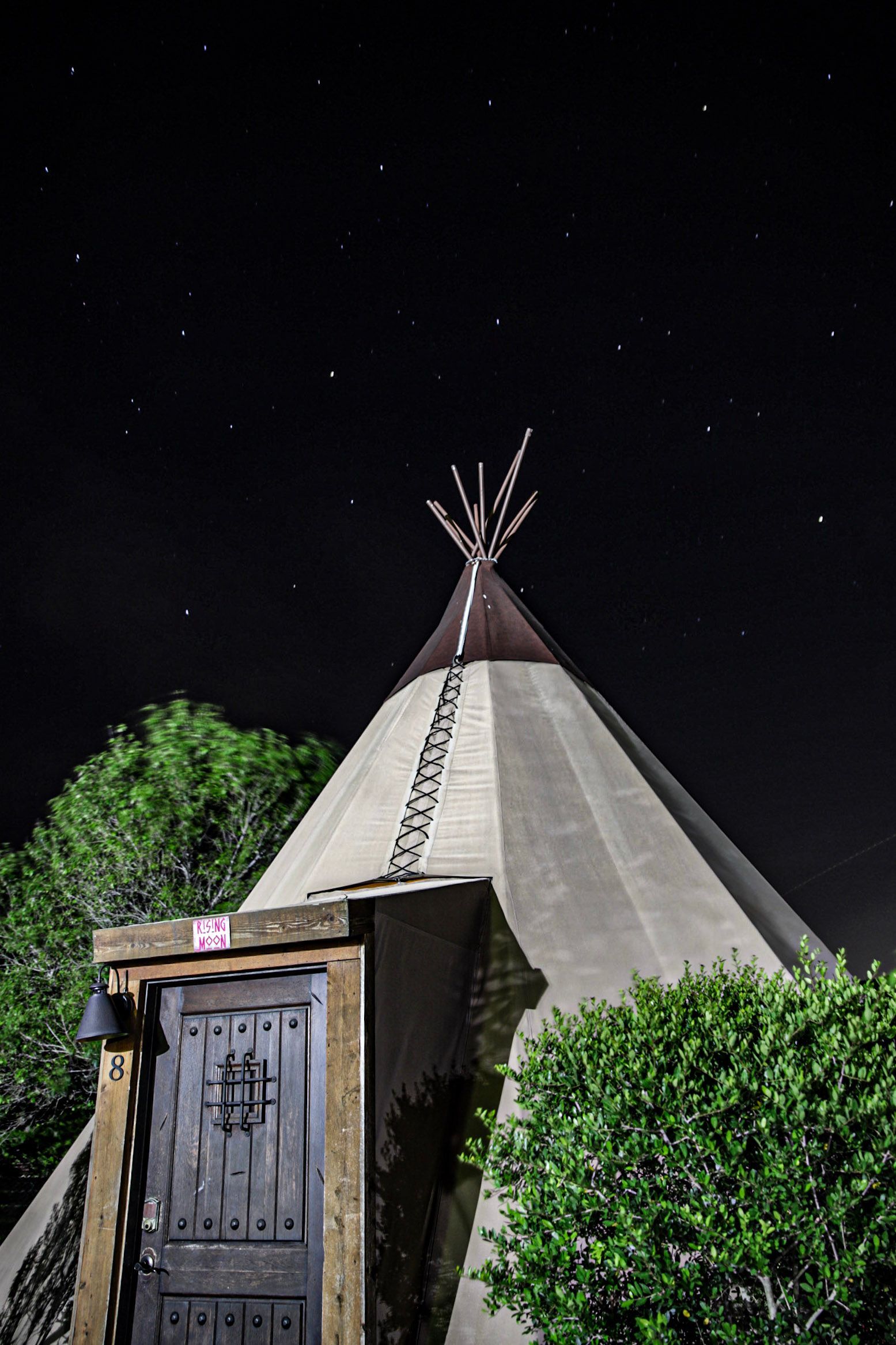 Teepee structure with wooden door under a starry night sky.