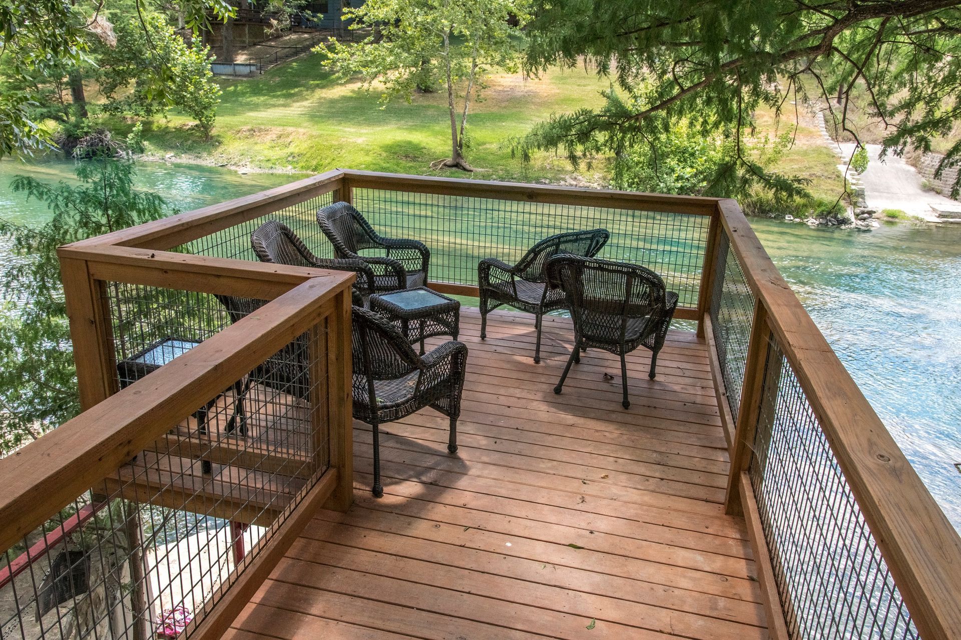 Wooden deck with chairs overlooking a river, framed by trees.