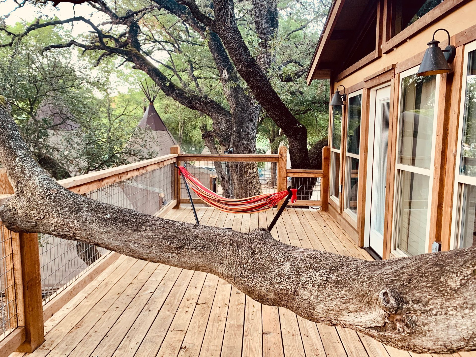 Treehouse with wooden deck, hammock, and large tree limb extending over the deck.