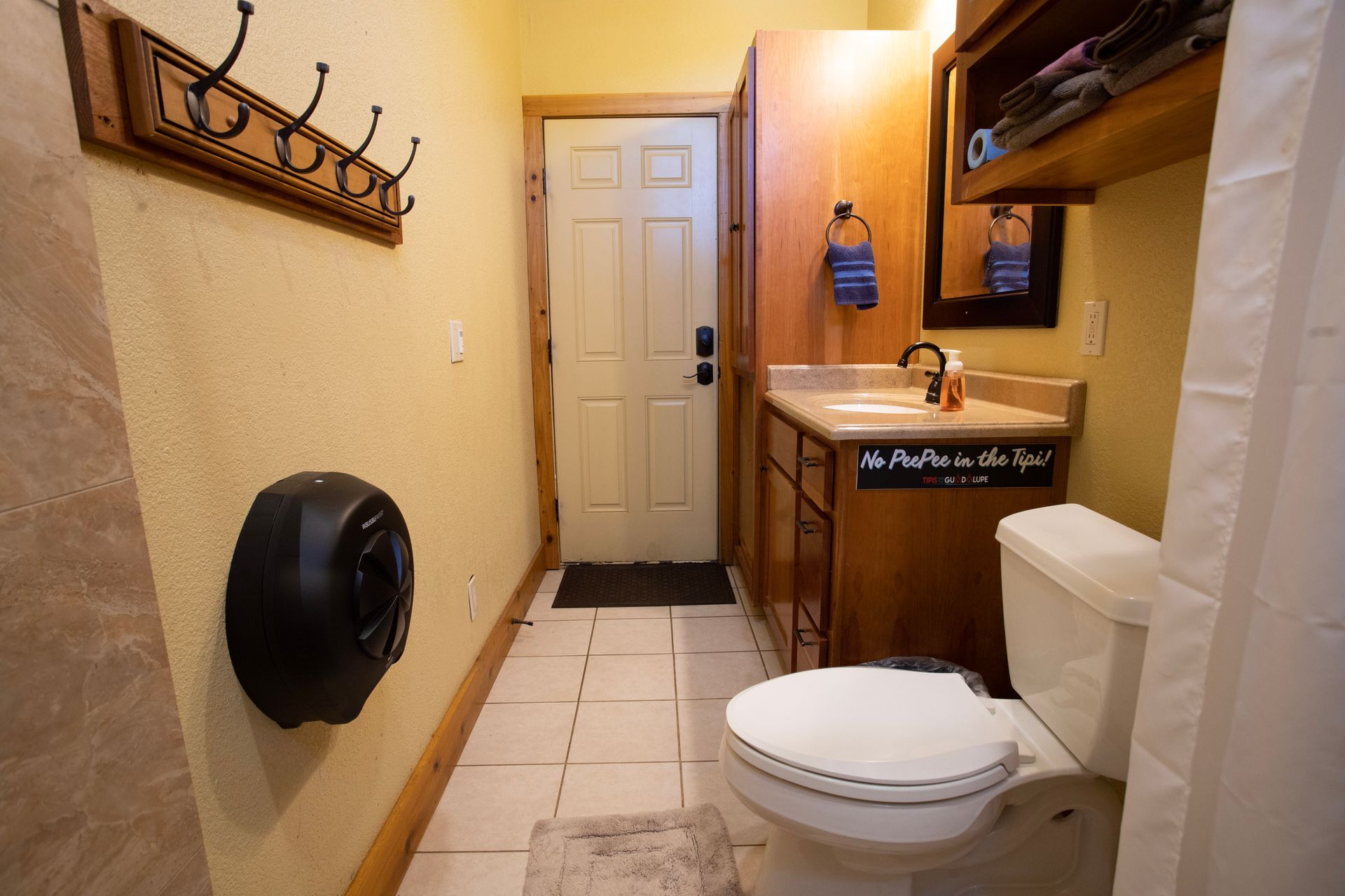 Bathroom with toilet, sink, and door; yellow walls, wood cabinets, light tile floor.