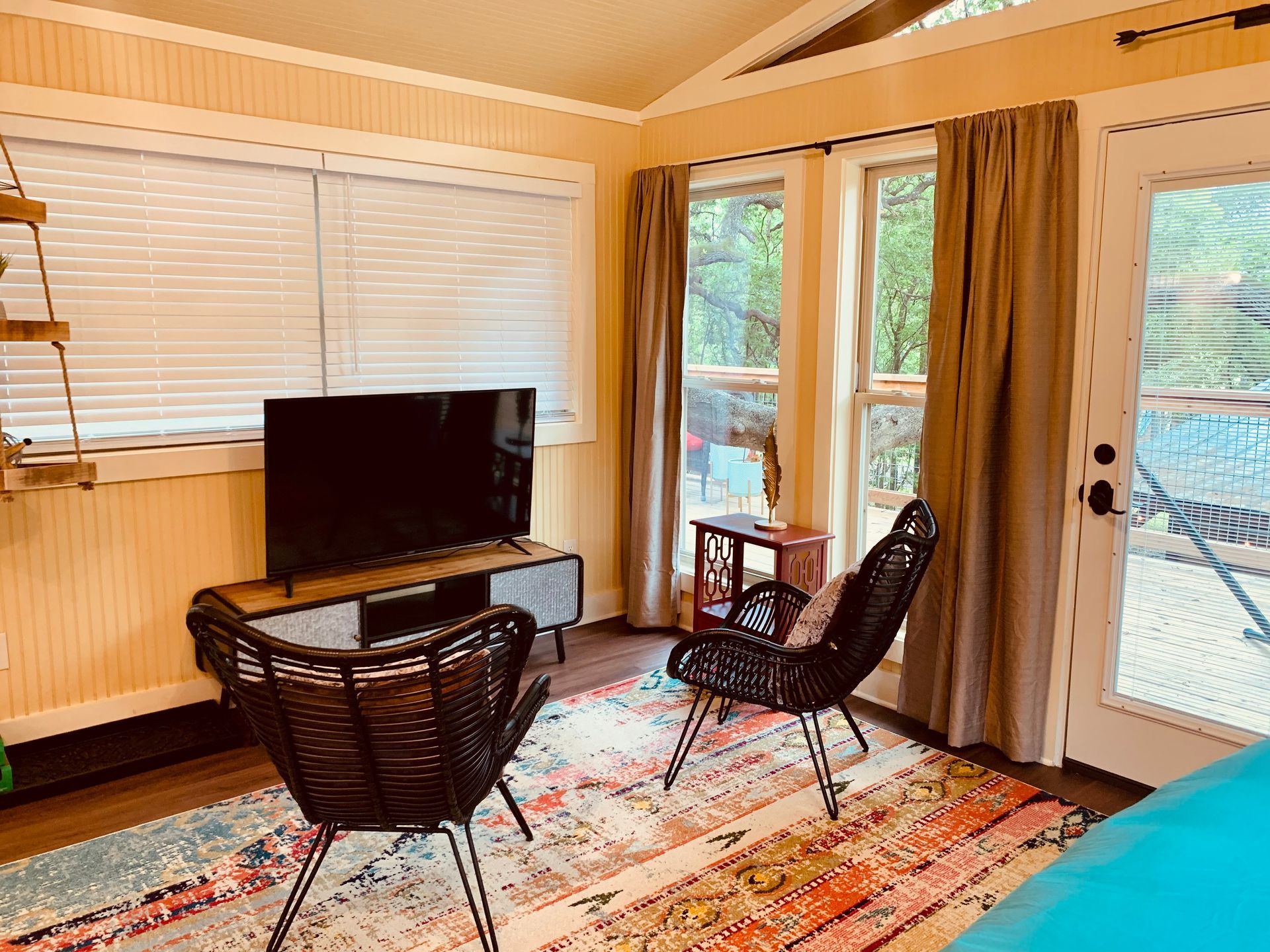 Living room with TV, chairs, rug, and windows overlooking trees.