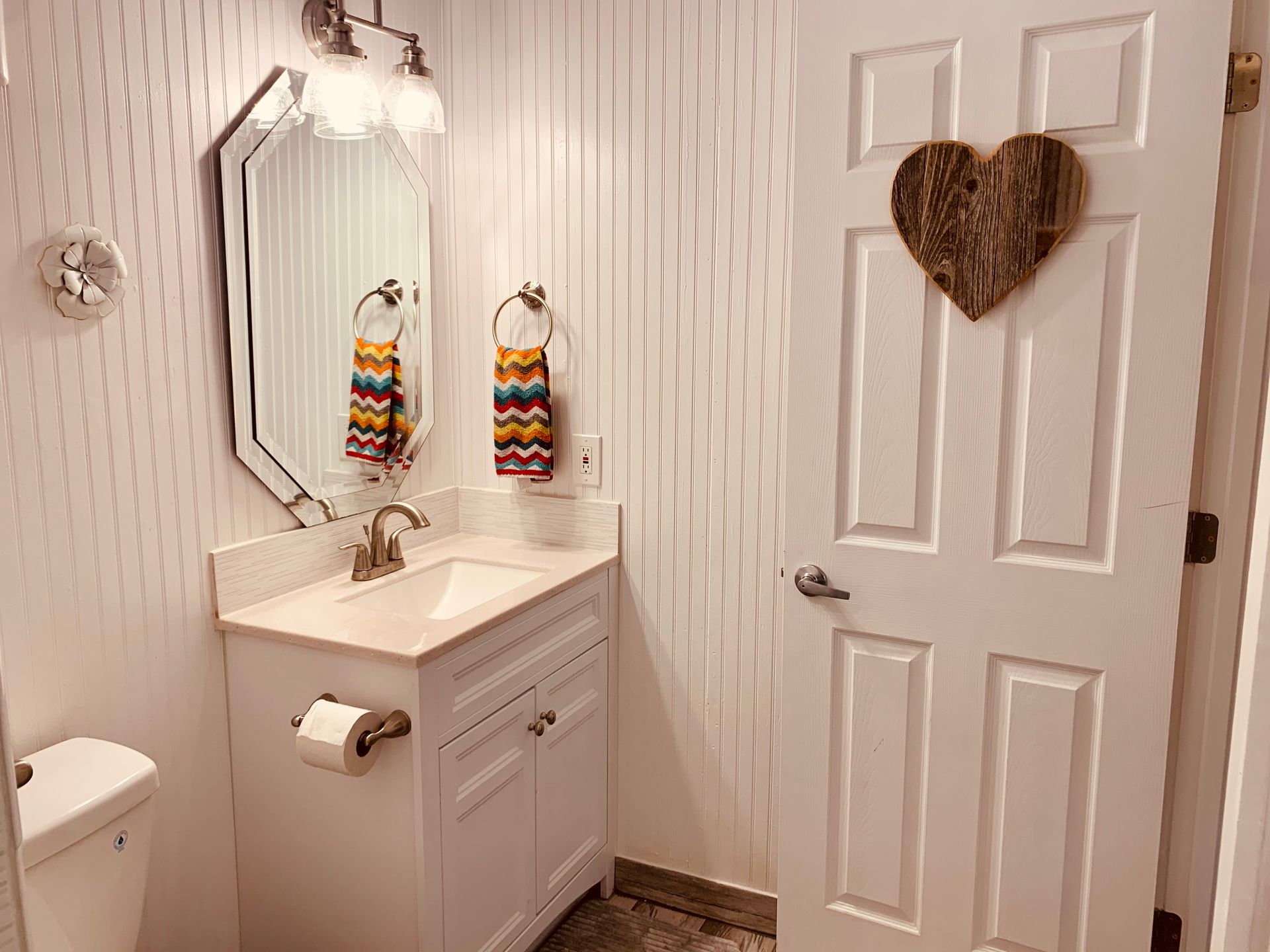 Small white bathroom with a sink, mirror, and a heart decoration on the door.