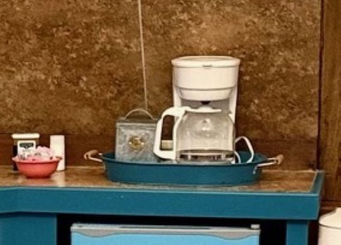 Coffee maker, sugar bowl, and tea box on a blue counter. Brown wall in the background.