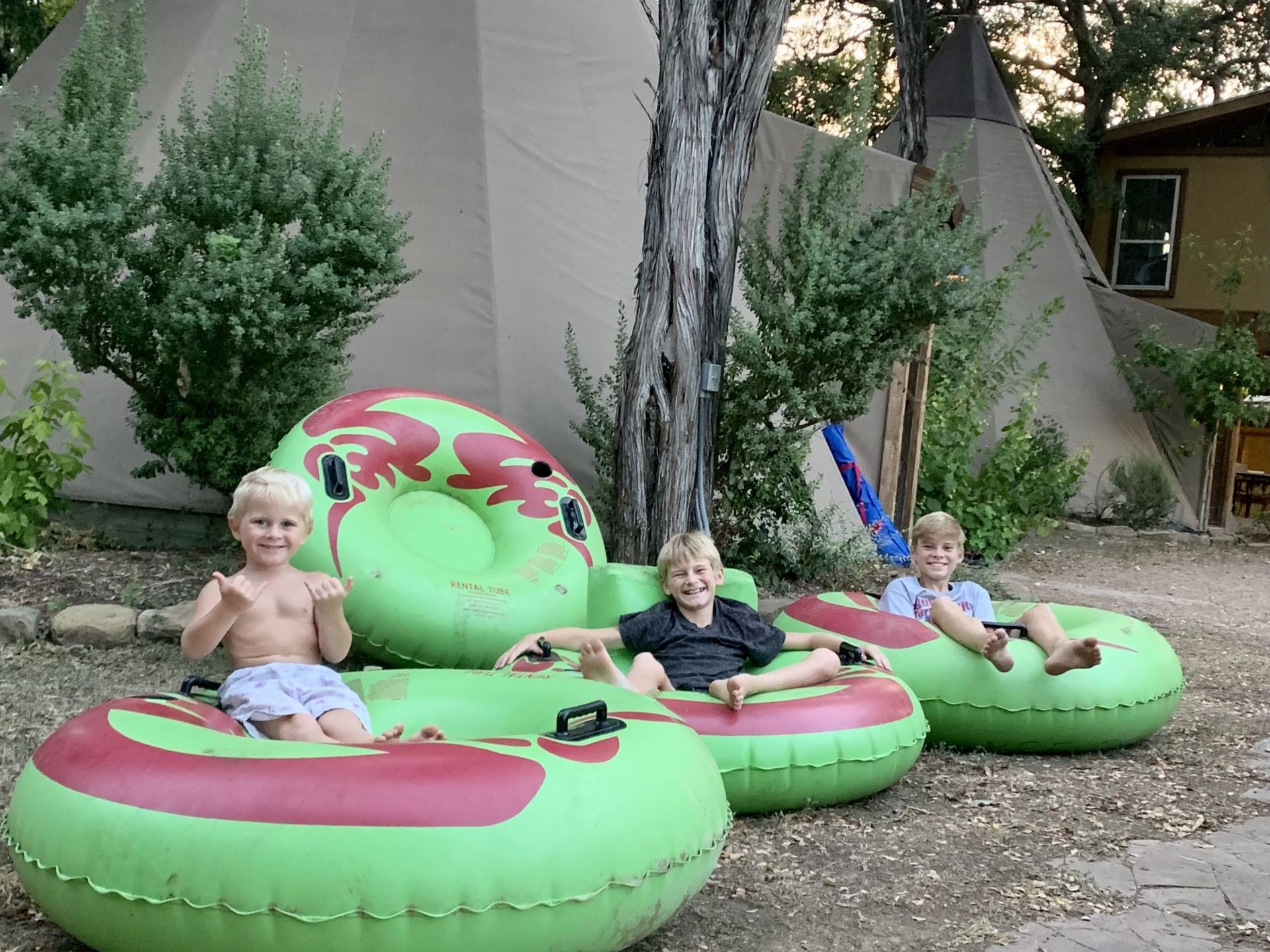 Three children in green and red inner tubes in front of a teepee.