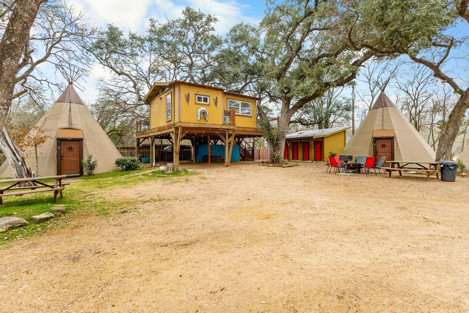 Campground with teepees, treehouse cabin, picnic tables, and trees.