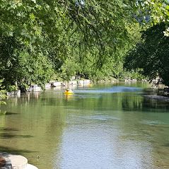 River scene with green trees, clear water, and a yellow paddleboat.