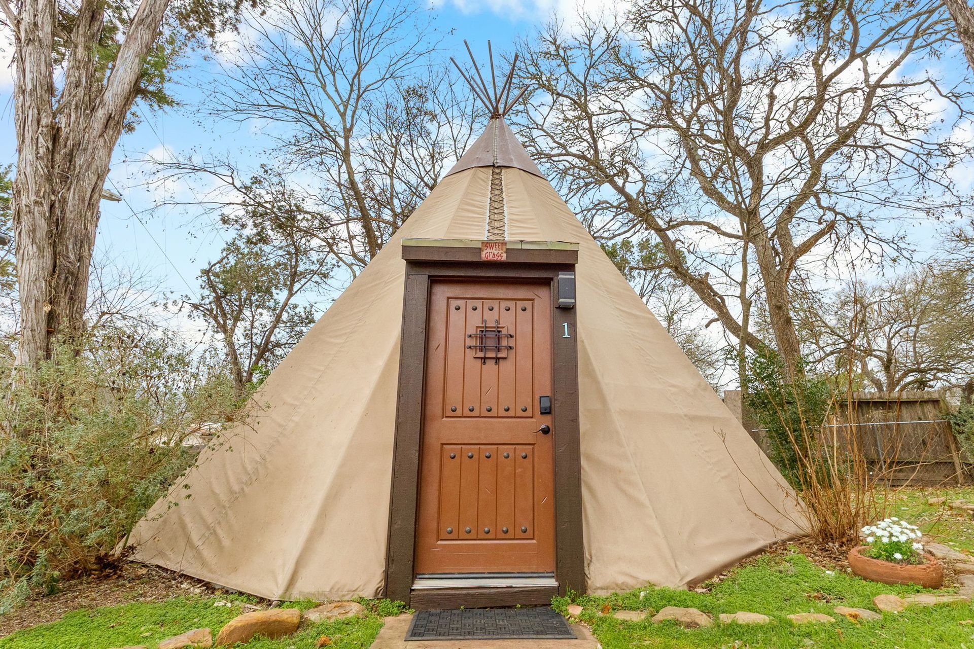 Beige teepee structure with brown wooden door, surrounded by trees and greenery.