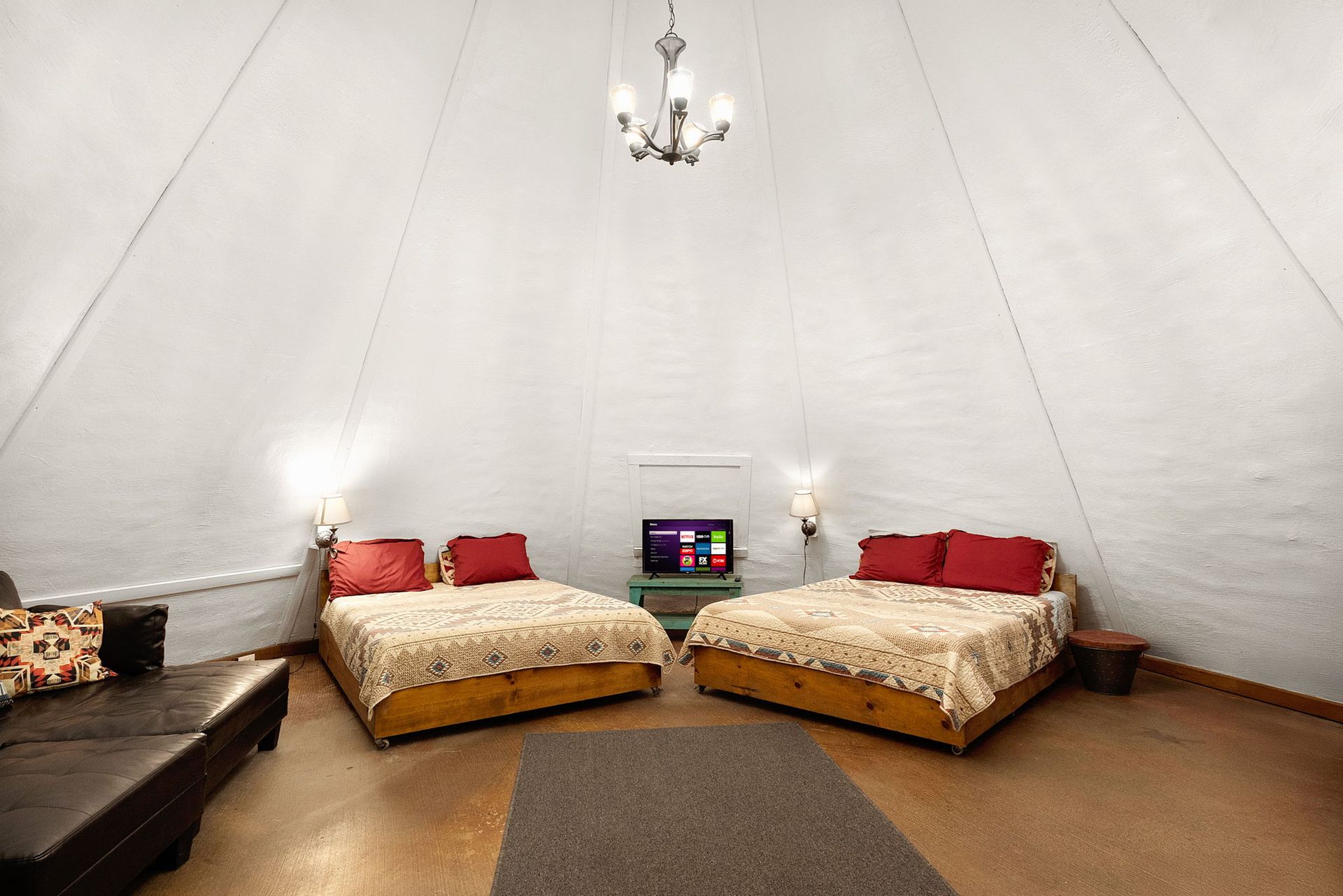 Interior of a white canvas tent with two beds, a TV, and a leather sofa.