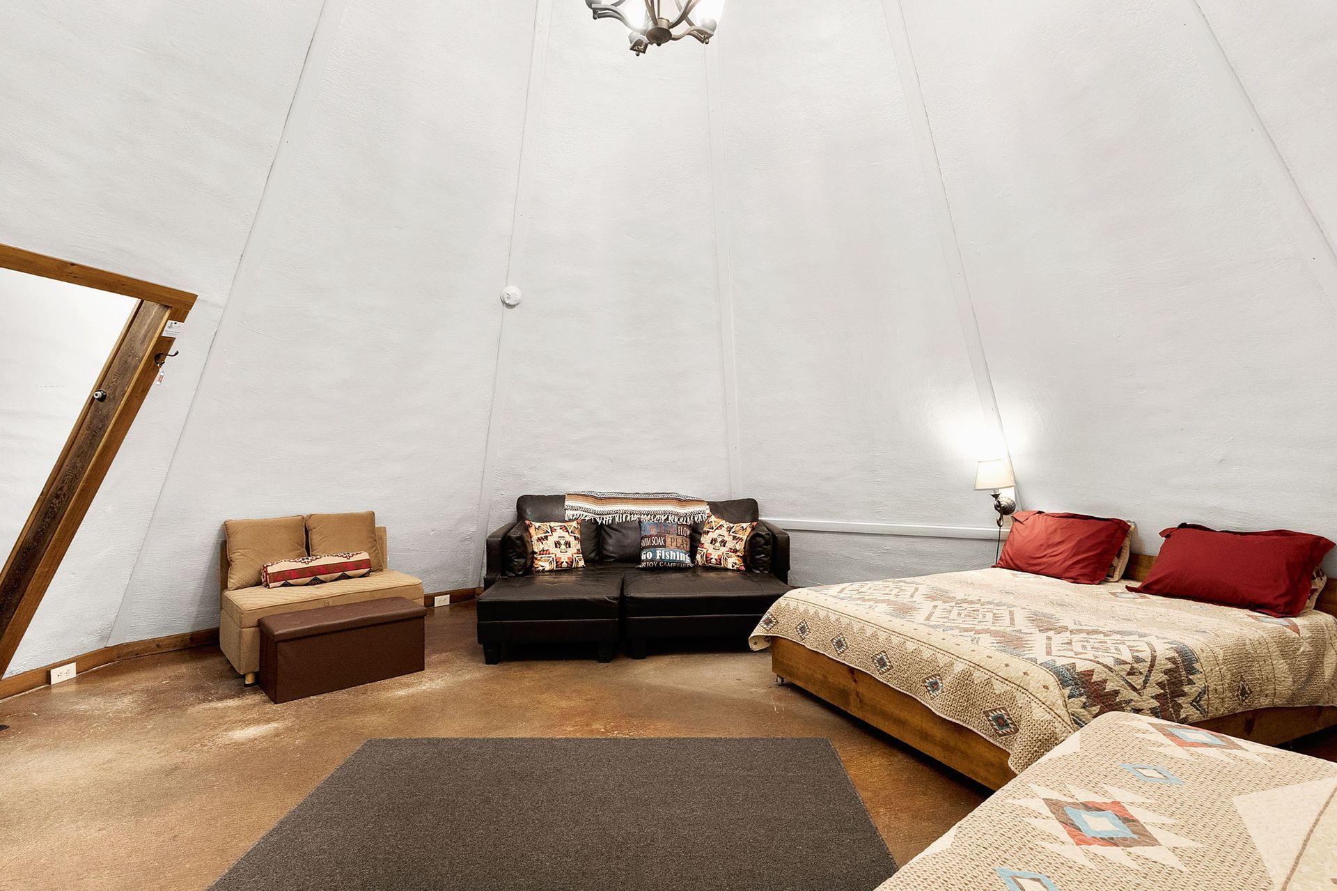 Spacious room with teepee-shaped white ceiling, featuring a bed, sofa, and armchair.