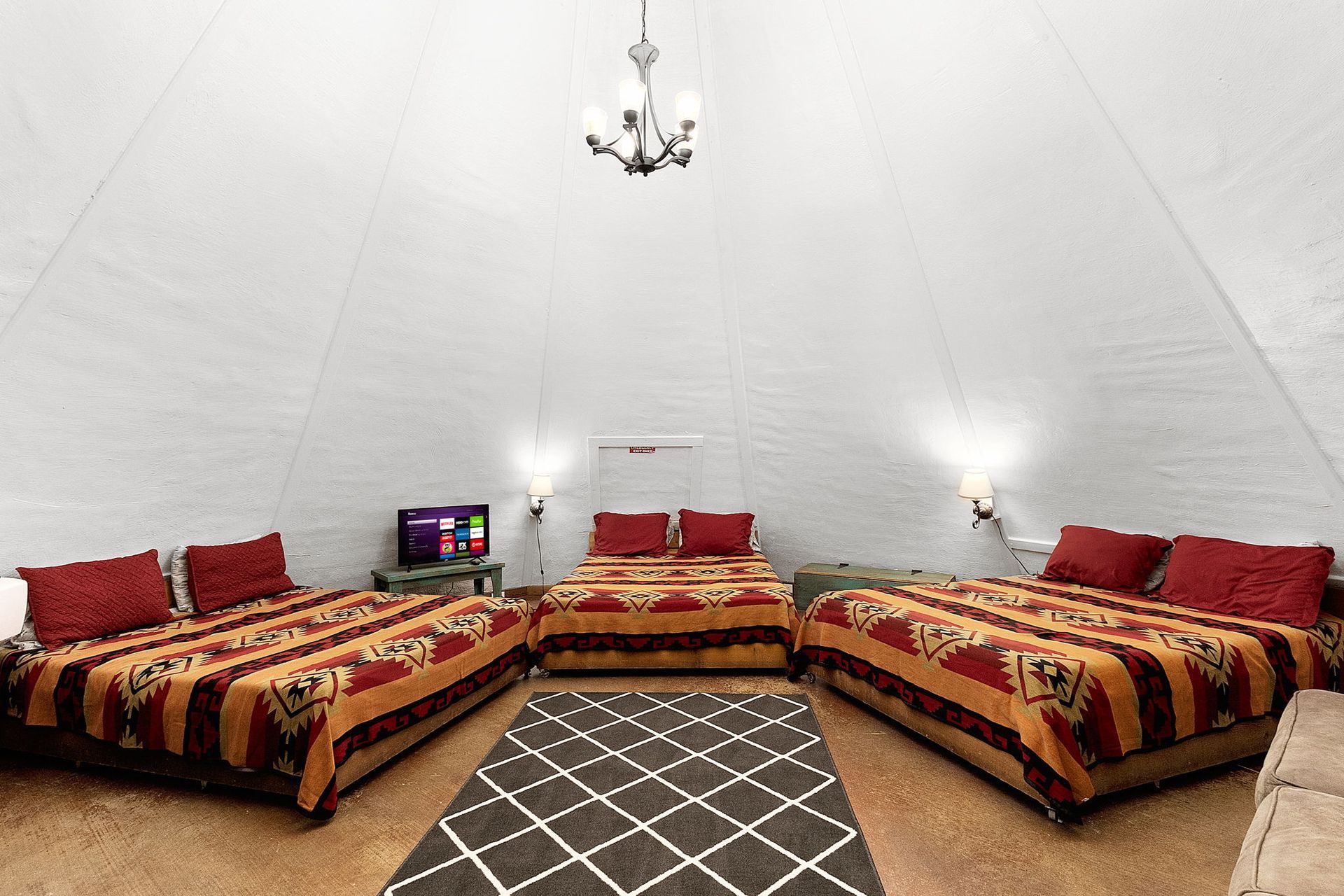 Interior of a large tent with three beds, a rug, and a television. A chandelier hangs from the white ceiling.
