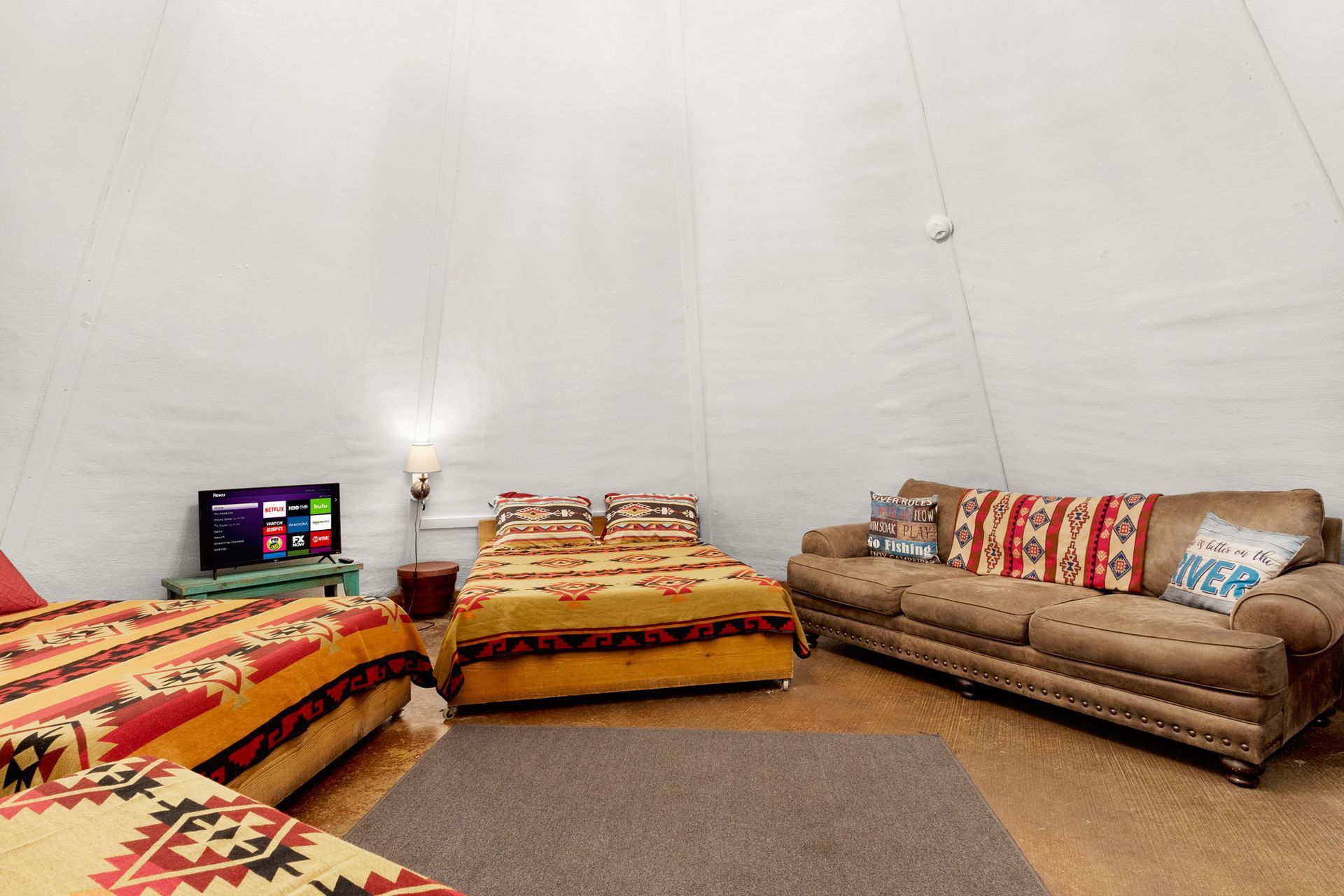 Interior of a tipi with beds, a couch, and a TV; decorated with Southwestern-style blankets and pillows.