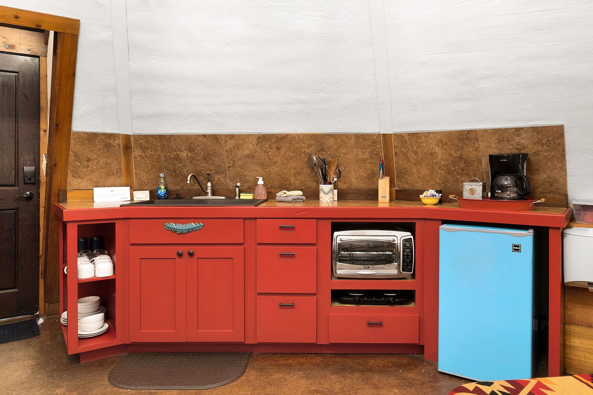 Red kitchen counter with sink, cabinets, small fridge, and appliances.