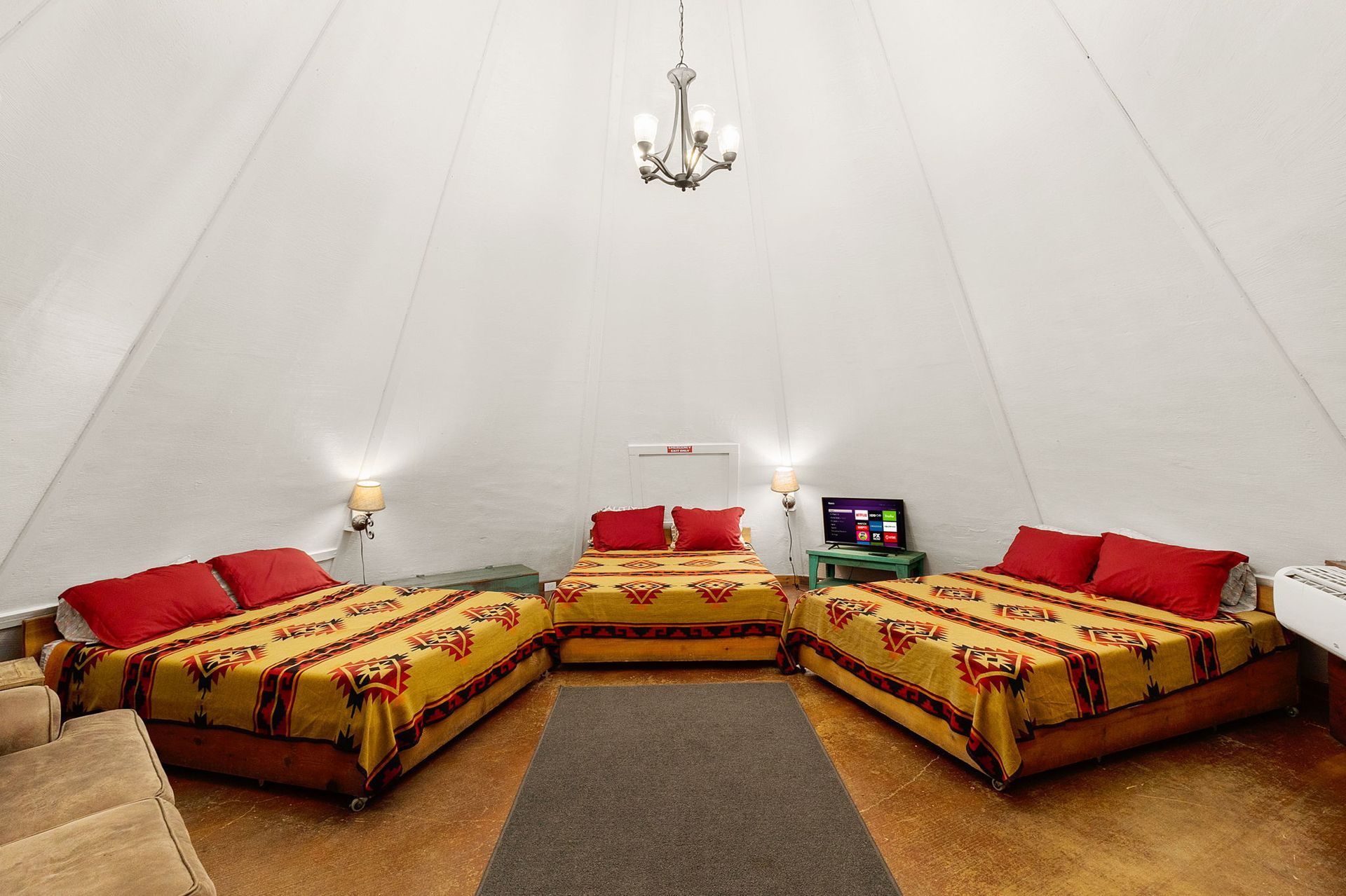 Interior of a teepee with three beds, a couch, a chandelier, and a TV.