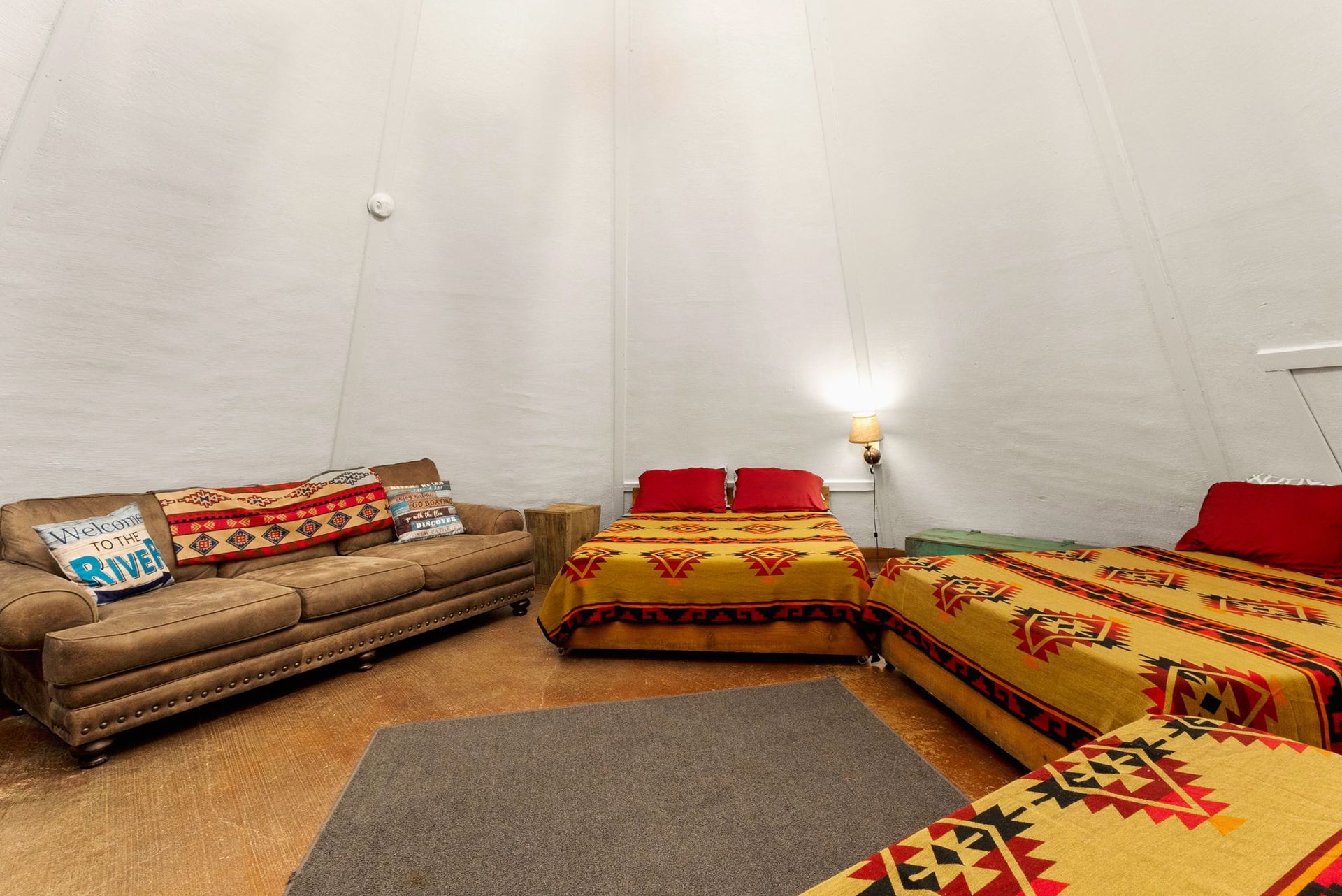 Interior of a teepee-style room with a sofa, multiple beds, and a rug.