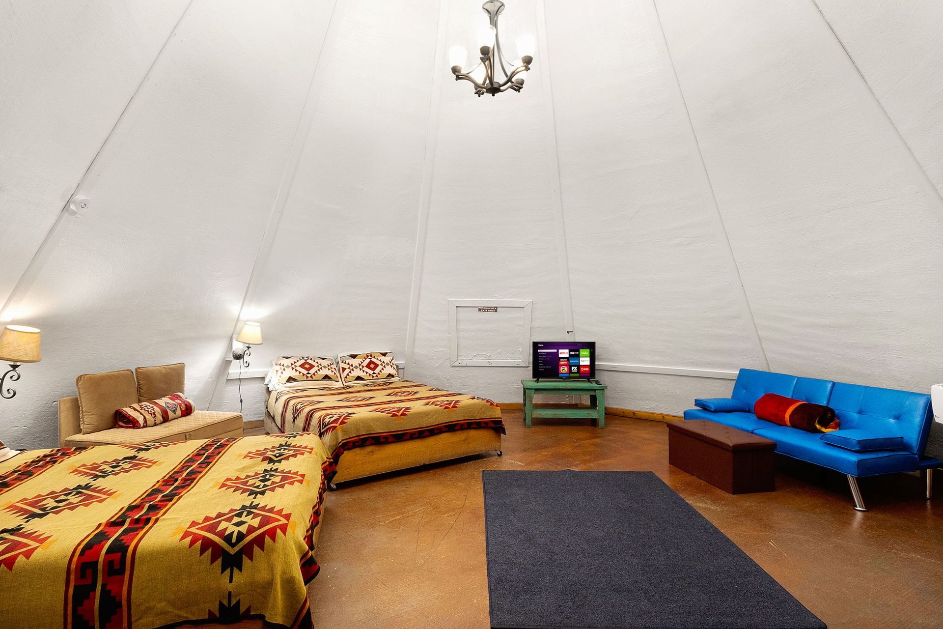 Interior of a large white teepee with beds, a blue couch, TV, and rug.