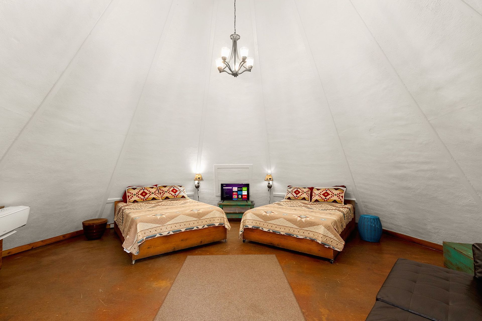 Interior of a tent with two beds, a small TV, and a chandelier hanging from the high ceiling.
