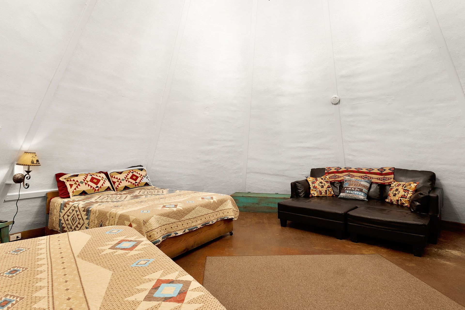 A domed room with beds, a sofa, and a rug. The walls are white and the furniture is brown with colorful blankets and pillows.