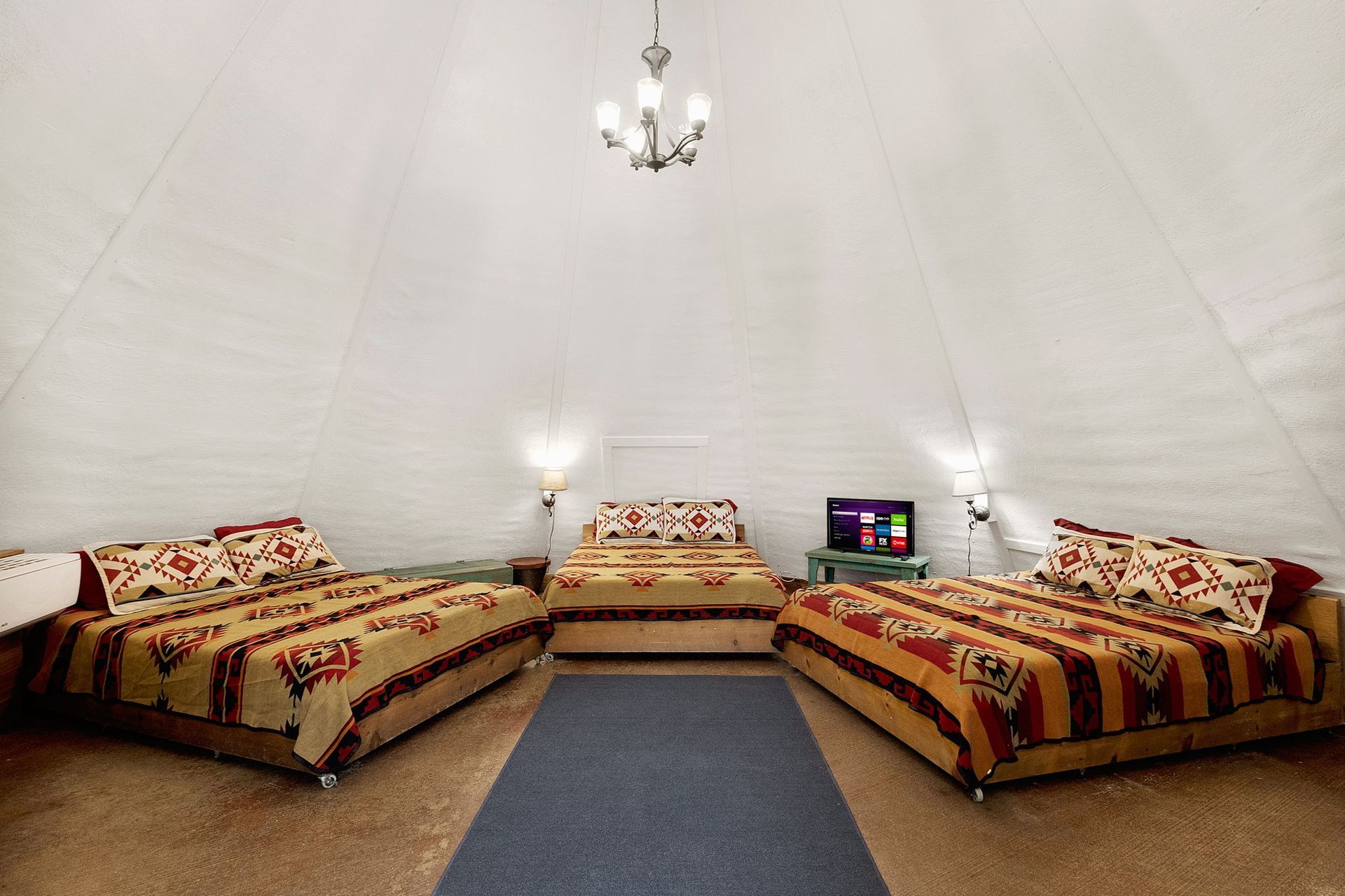 Interior of a white, conical tent with three beds, a rug, and a TV.