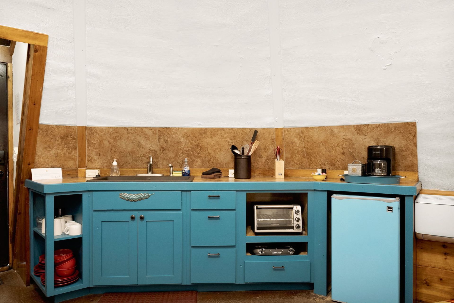 Blue kitchen cabinets with a sink, microwave, small refrigerator, and coffee maker.