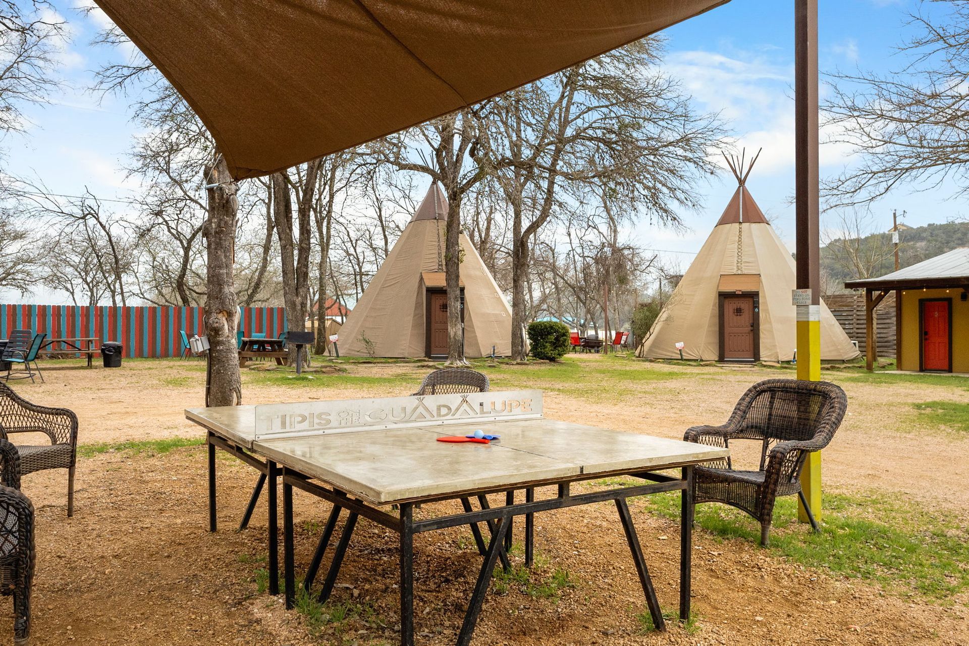 Outdoor scene with a ping pong table, teepees, and seating under a shade.