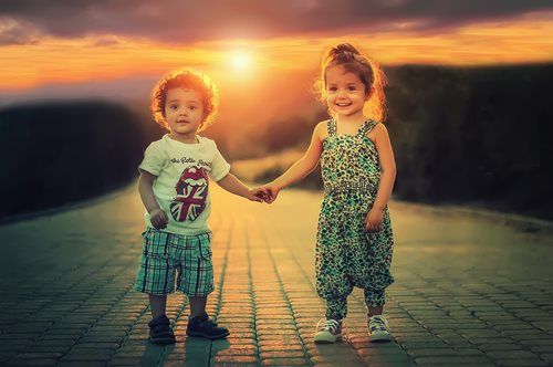 Two children holding hands on a path at sunset.