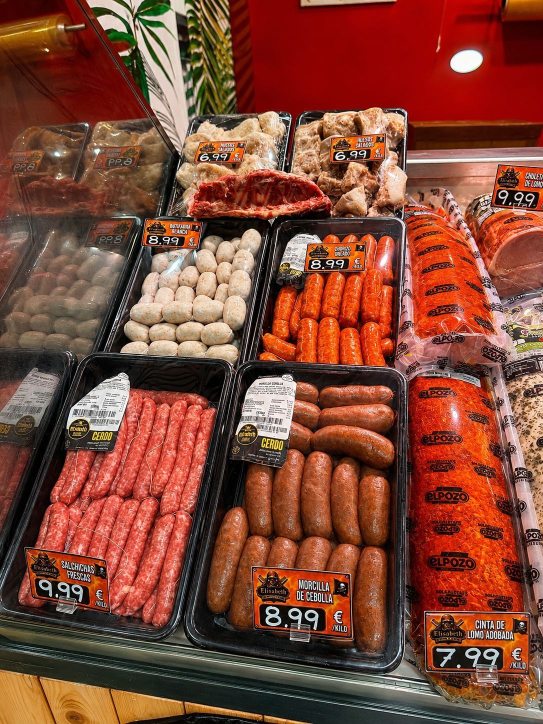 Variedad de embutidos y carnes expuestos en una vitrina de charcutería, con sus respectivas etiquetas de precio.