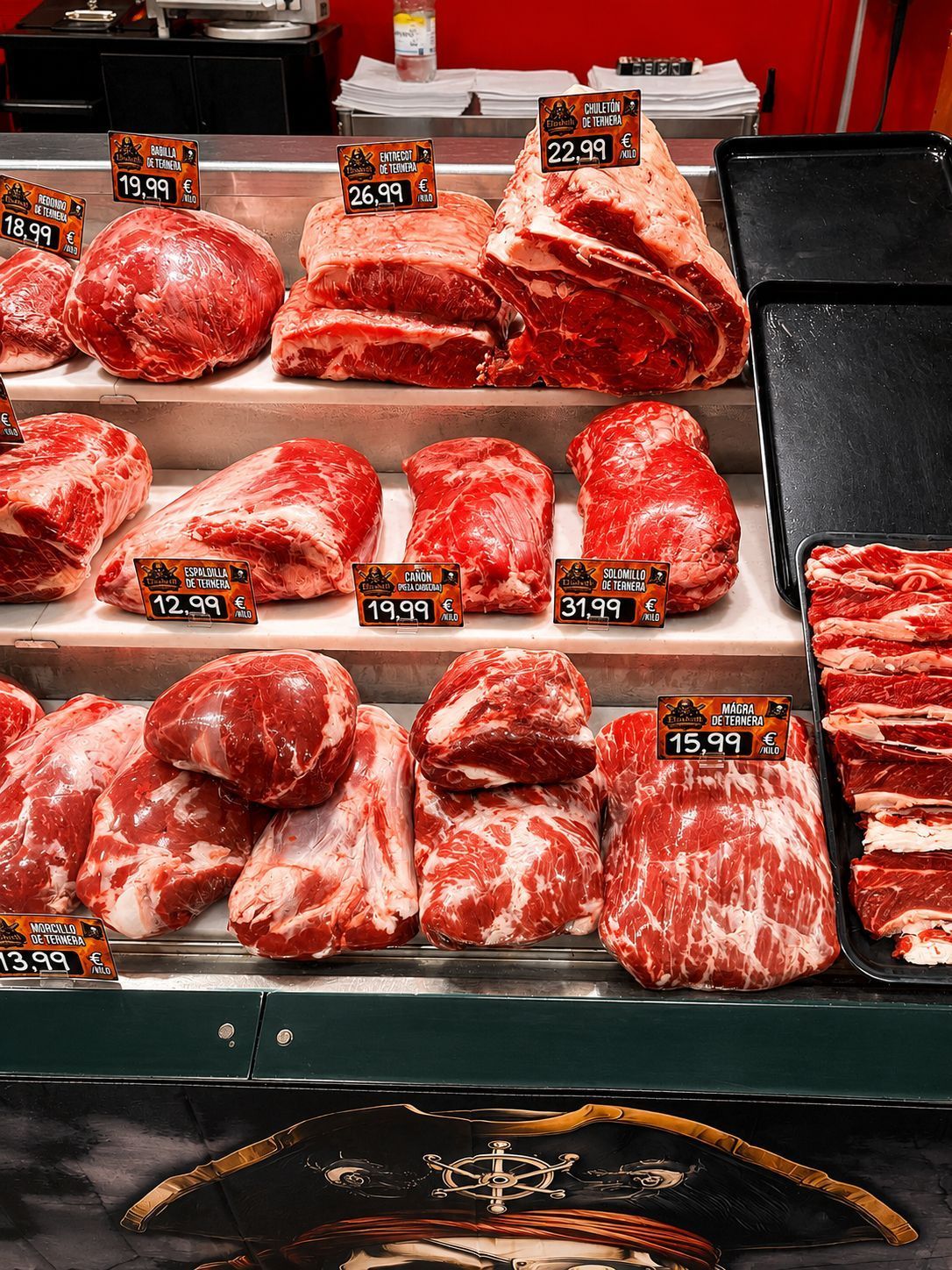 Exhibición de cortes de carne cruda veteada con etiquetas de precio en una vitrina de carnicería.