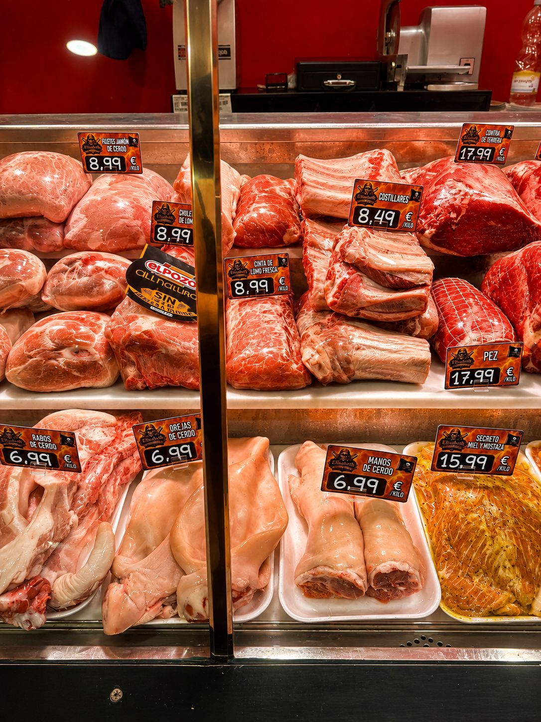 Exhibición de carnes marinadas variadas en bandejas con etiquetas de precio en una carnicería.