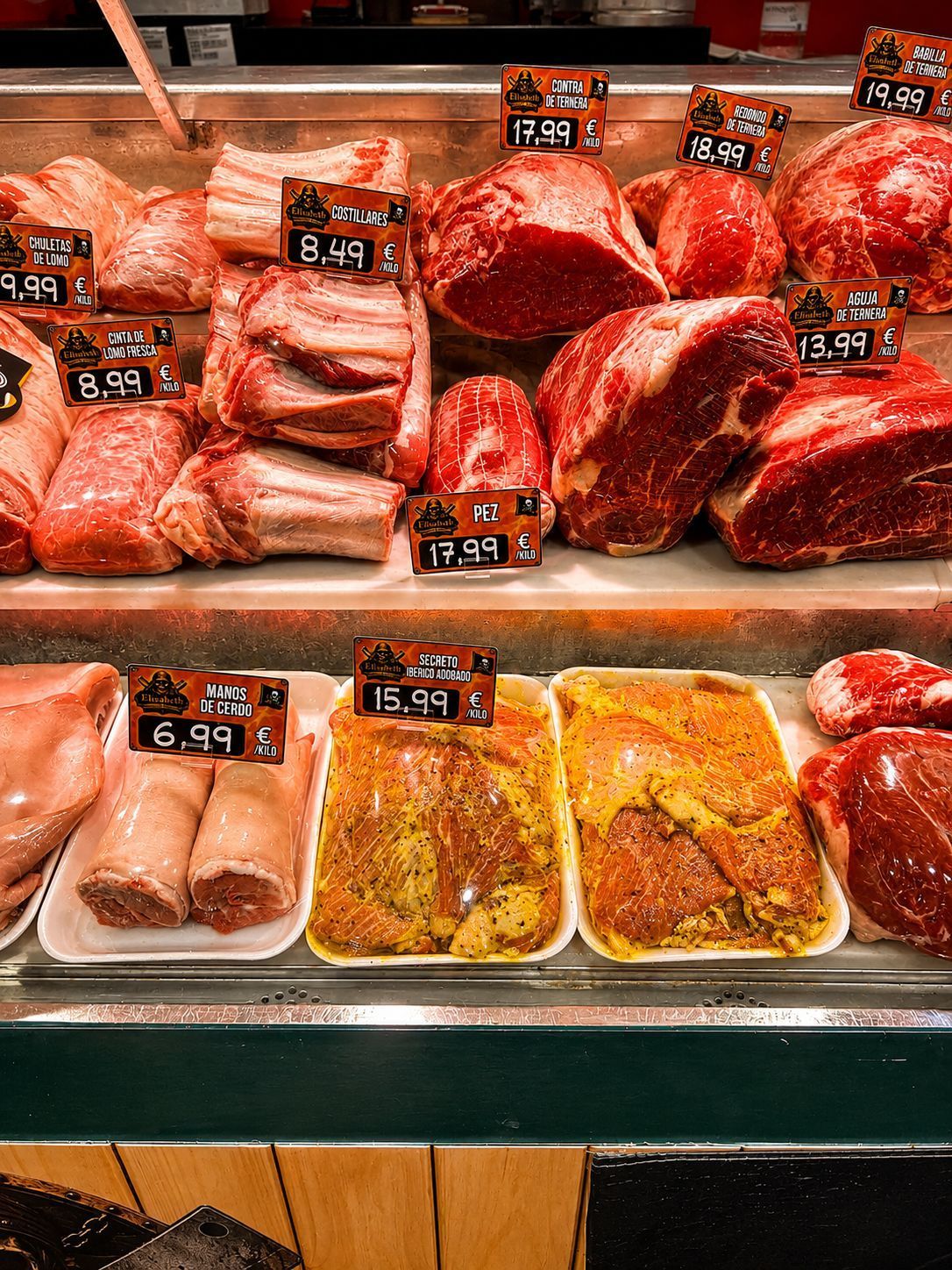 Exhibición de carnicería con surtido de carnes crudas y etiquetas de precio en una vitrina refrigerada.