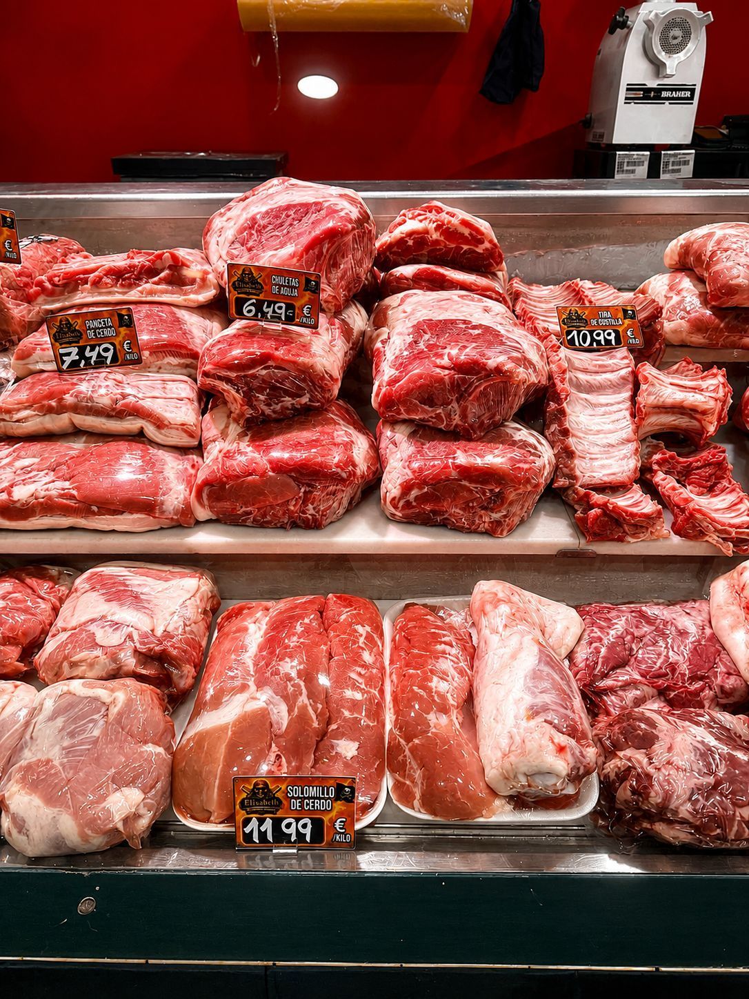 Exhibición de carnicería con pilas de cortes de carne cruda en bandejas en una vitrina refrigerada.