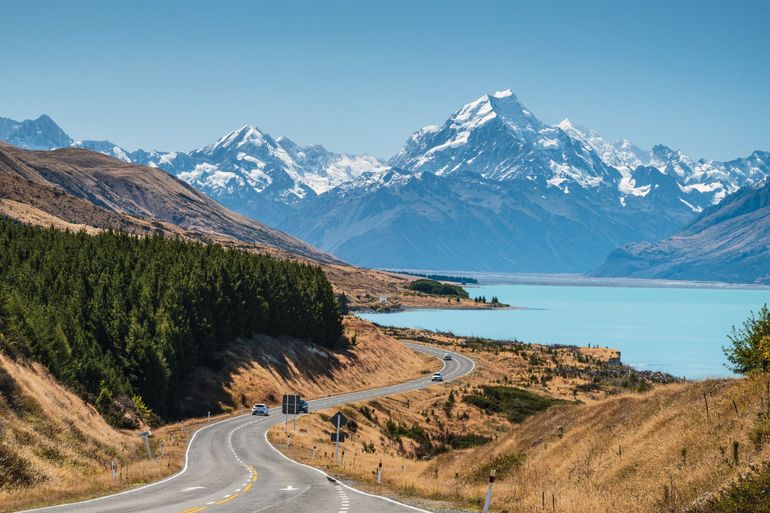 A road with mountains in the background and a lake in the foreground.