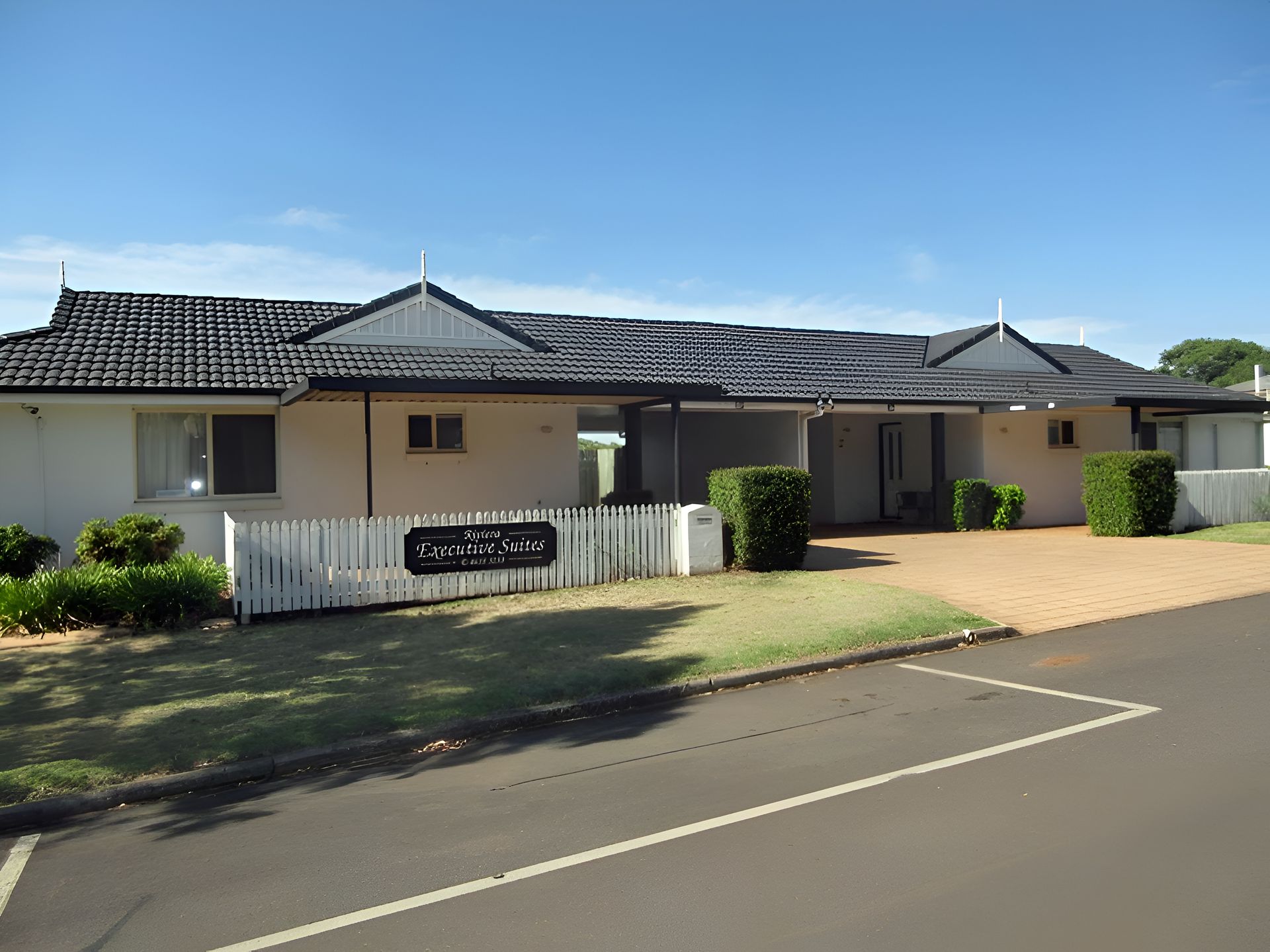 Single-story suburban house with a tiled roof, front lawn, and driveway on a sunny street