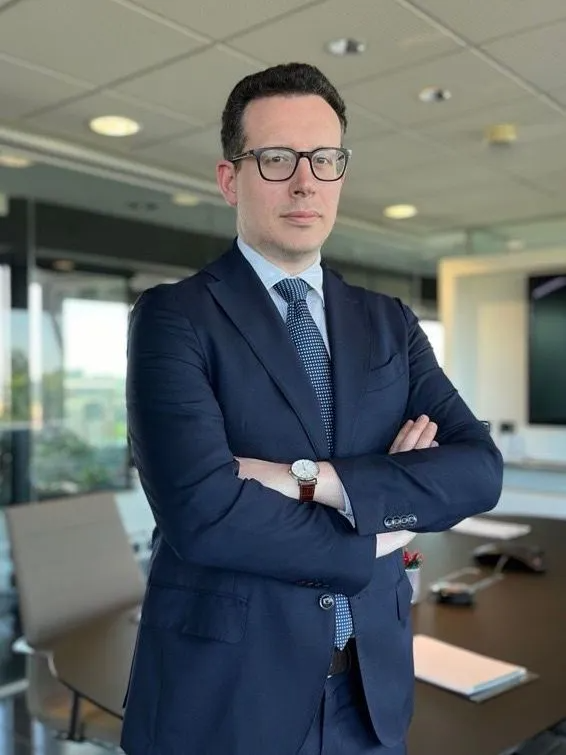Un uomo in abito scuro è in piedi con le braccia incrociate in una moderna sala conferenze di un ufficio.