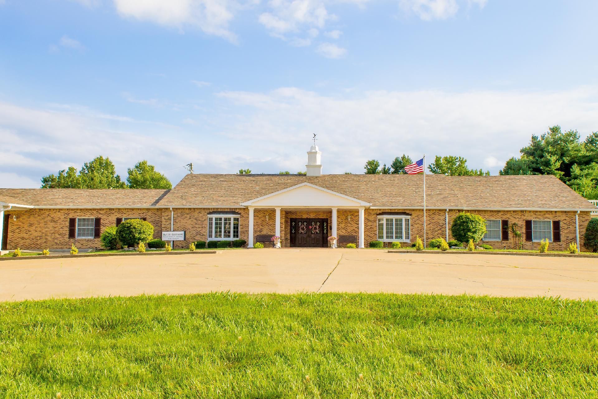 Single-story brick building with a central entrance, set behind a wide grassy lawn under a blue sky.