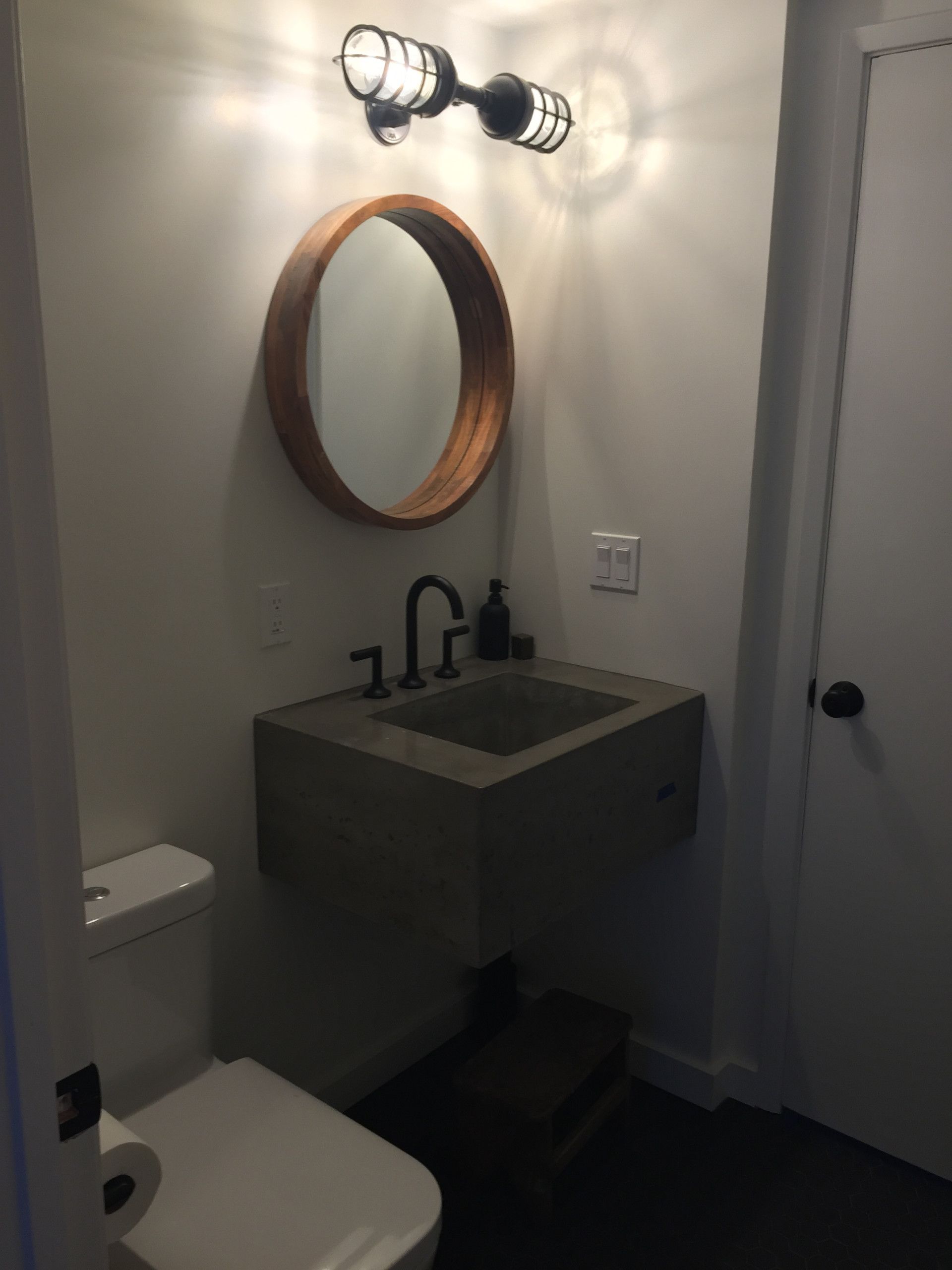 Small bathroom with concrete sink, round mirror, and industrial-style lighting.