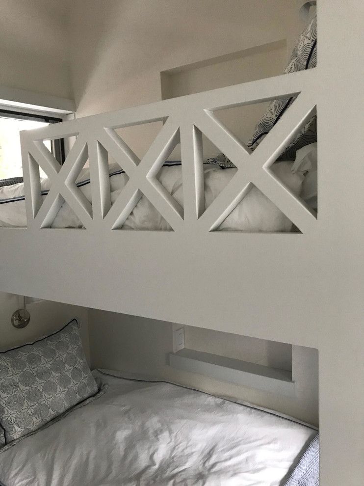 White bunk beds with an X-pattern safety rail. A gray and white patterned pillow rests on the bottom bunk.