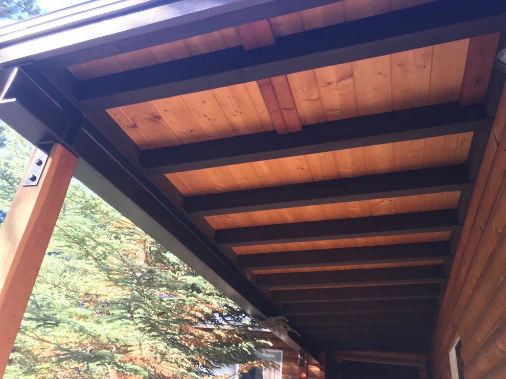Wooden porch ceiling with dark beams and light-colored planks, attached to a brown wooden support.