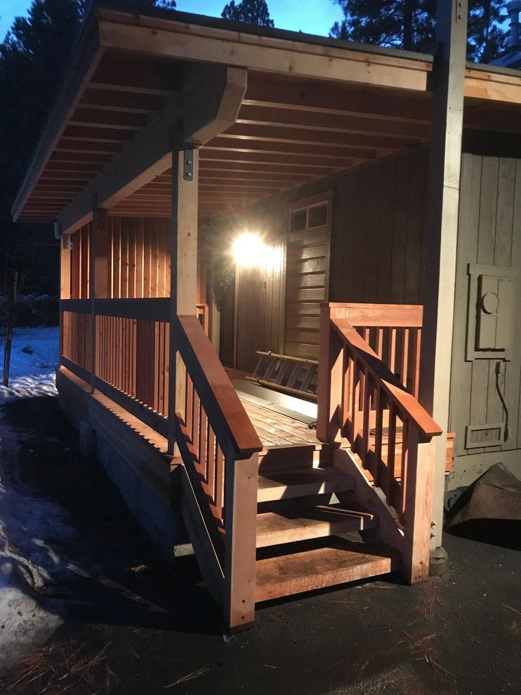 Wooden porch with steps, railing, and overhanging roof. Lit by an overhead light.